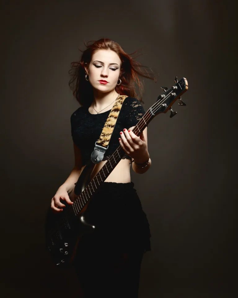 Woman playing bass guitar passionately against dark background.