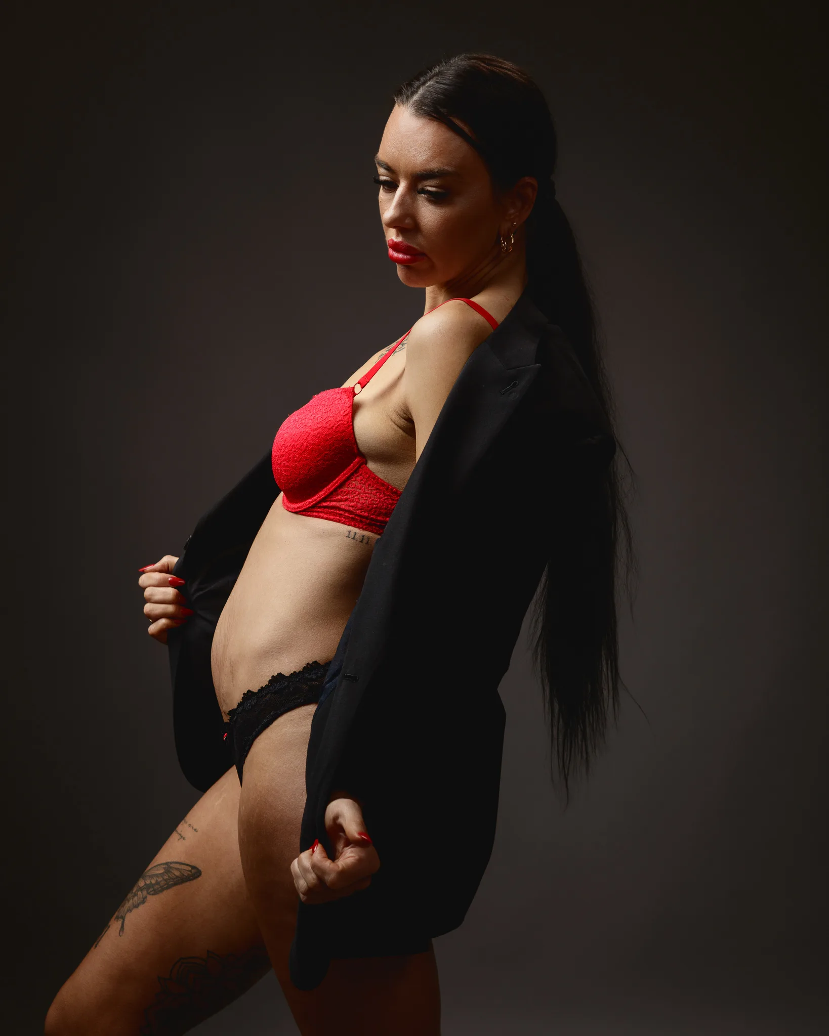 Woman posing in red lingerie and black jacket.