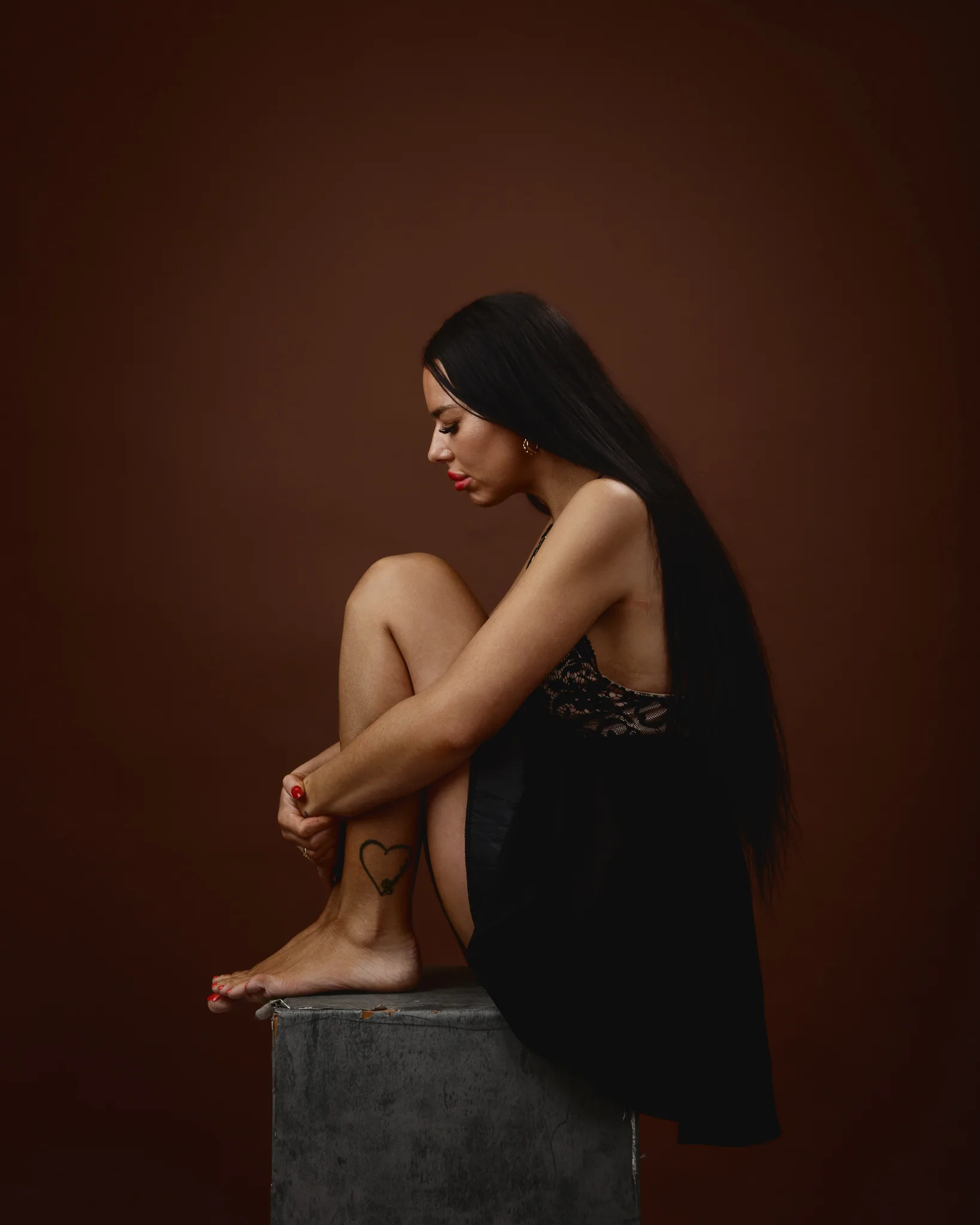Woman in black dress sitting on stool.