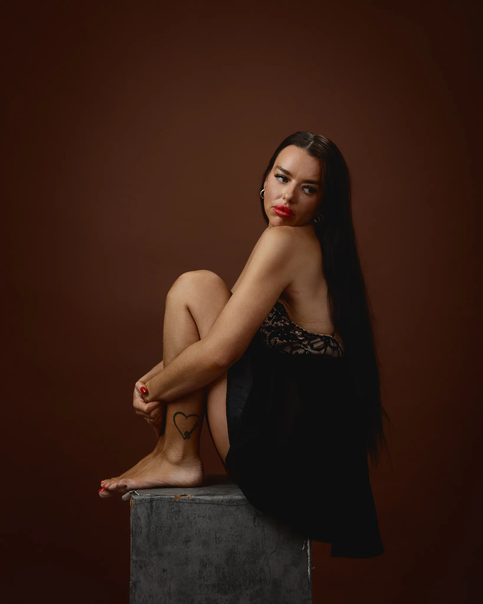Woman seated on concrete block, brown background.