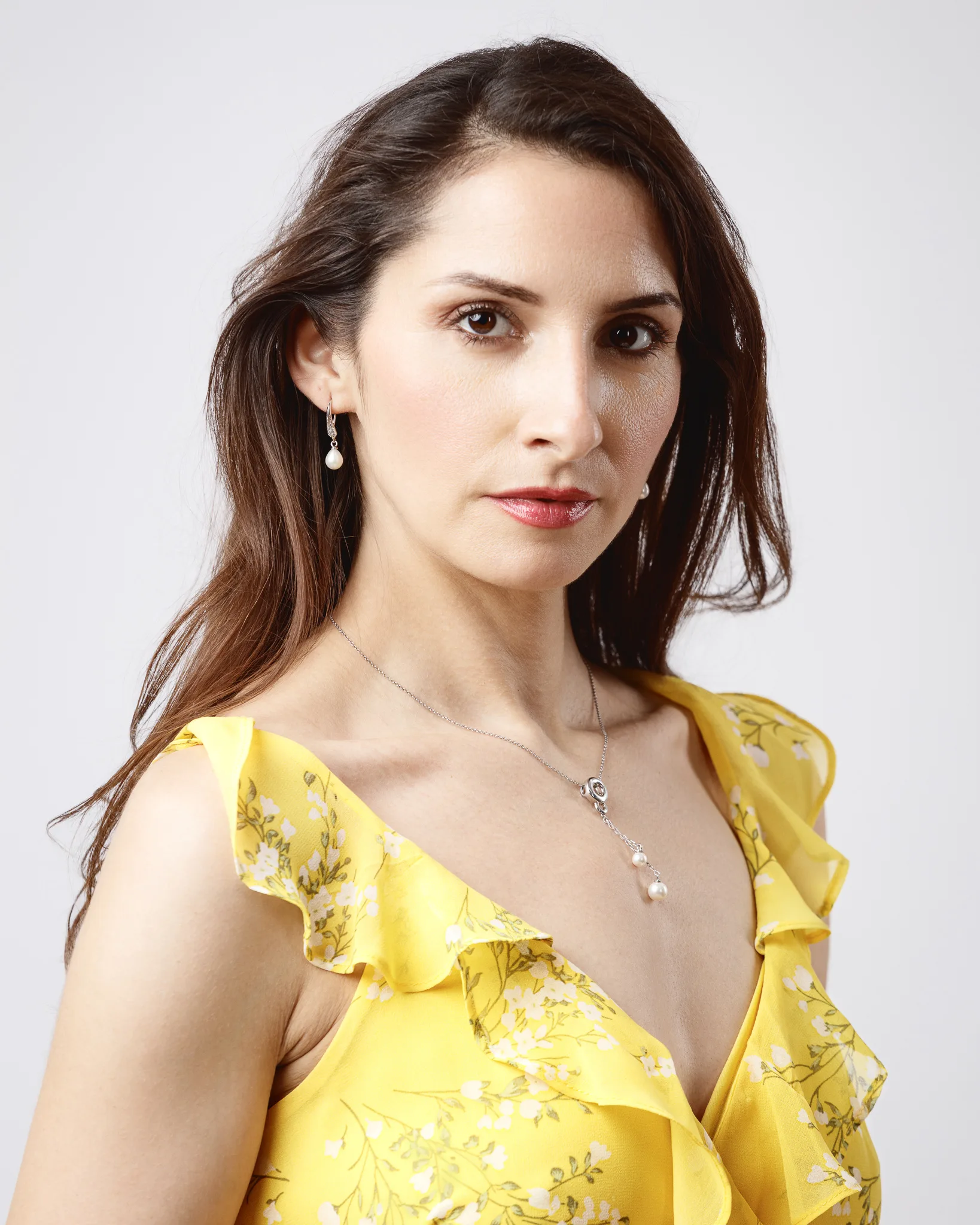 Woman in yellow floral dress with pearl jewelry.