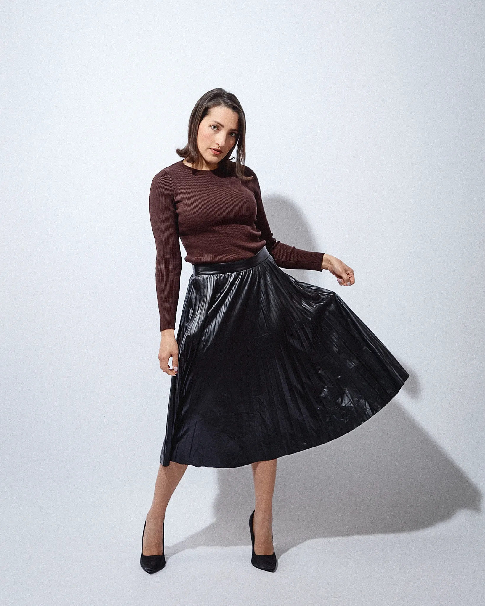 Woman in brown ribbed jumper and black pleated skirt.