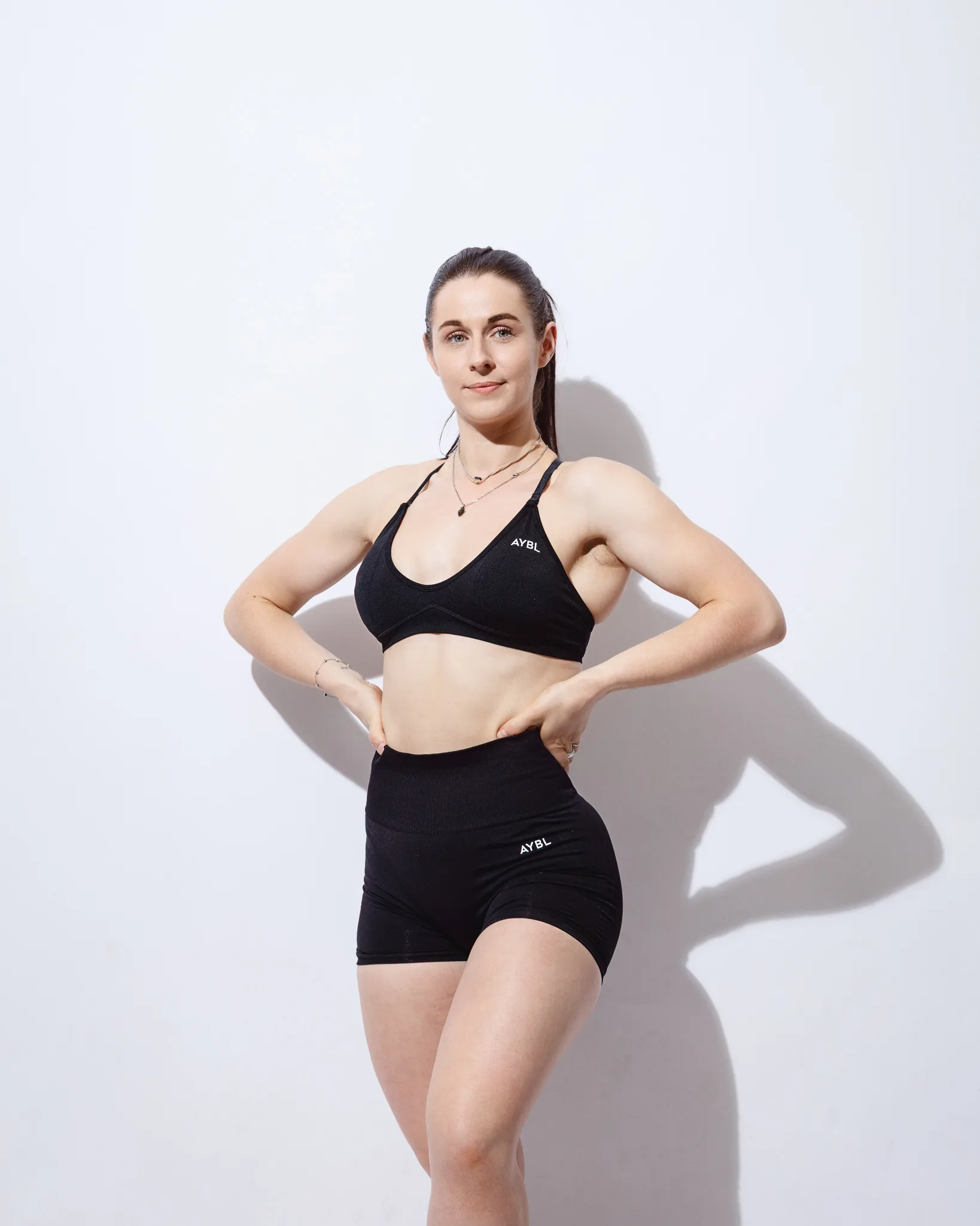 Woman in black sportswear posing against white wall