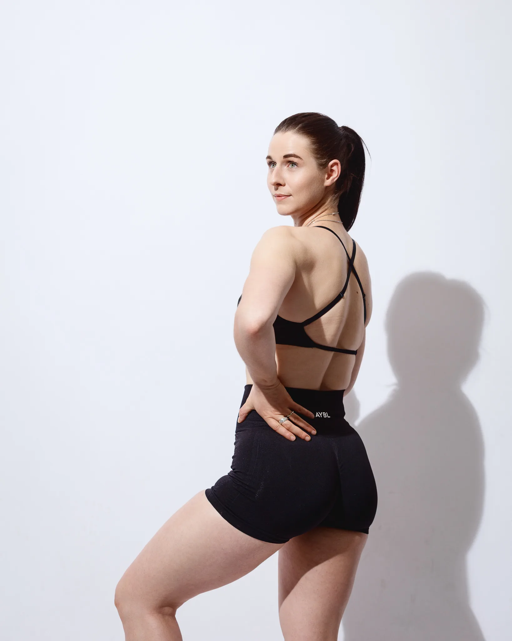 Woman in black sportswear posing against white wall