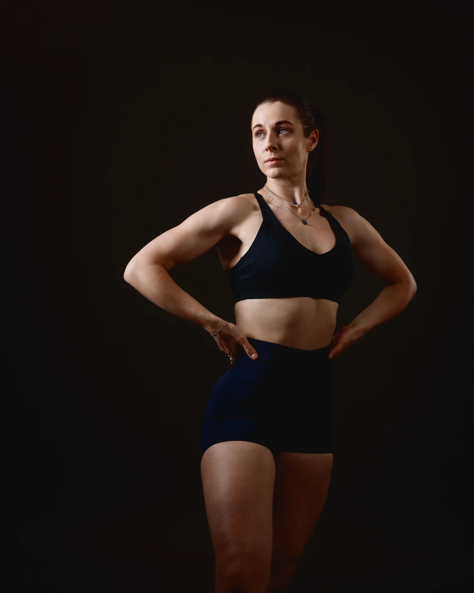 Woman in black sportswear posing against dark background