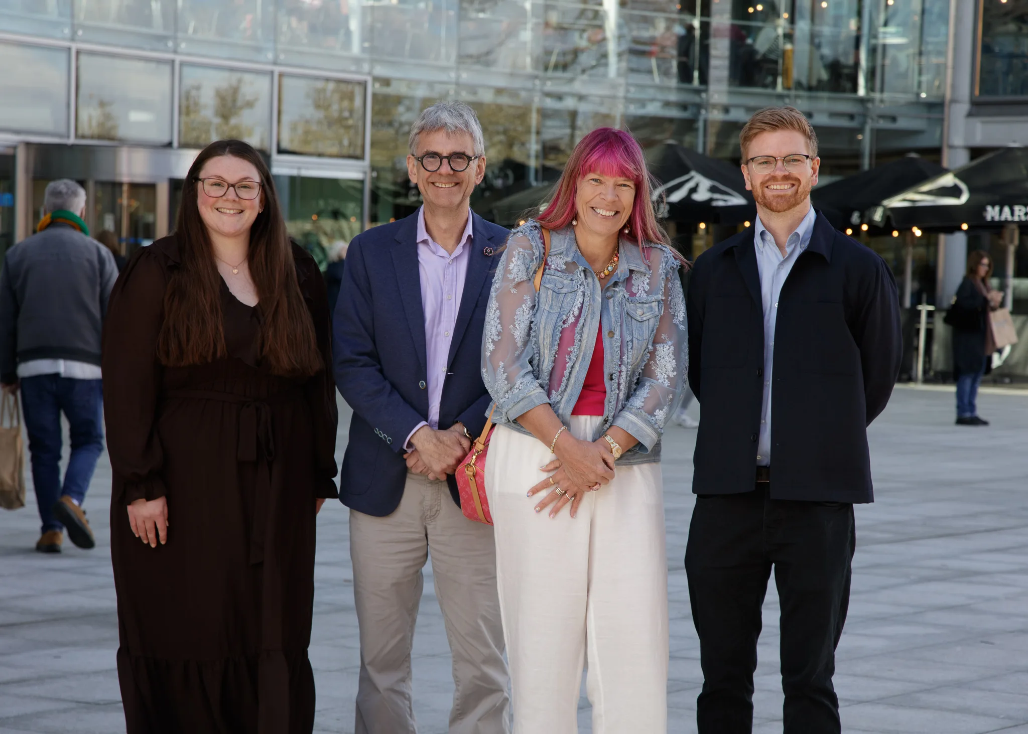 Four adults smiling outside modern glass building