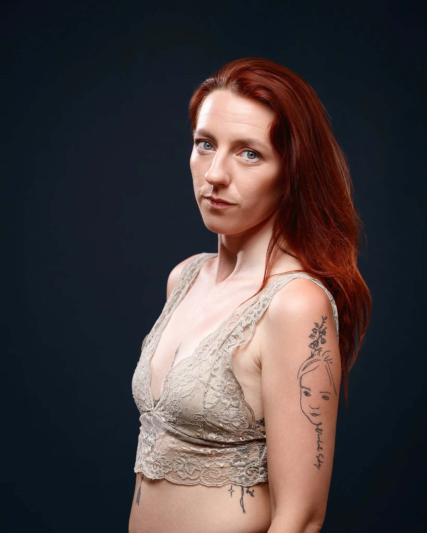 Red-haired woman with arm tattoo against dark background