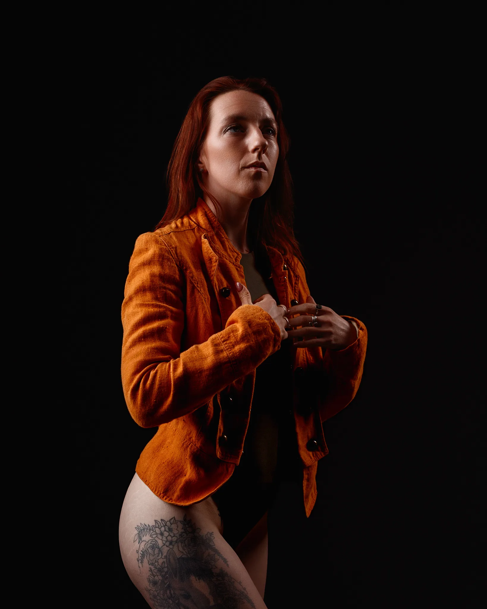 Red-haired woman in orange jacket against black background