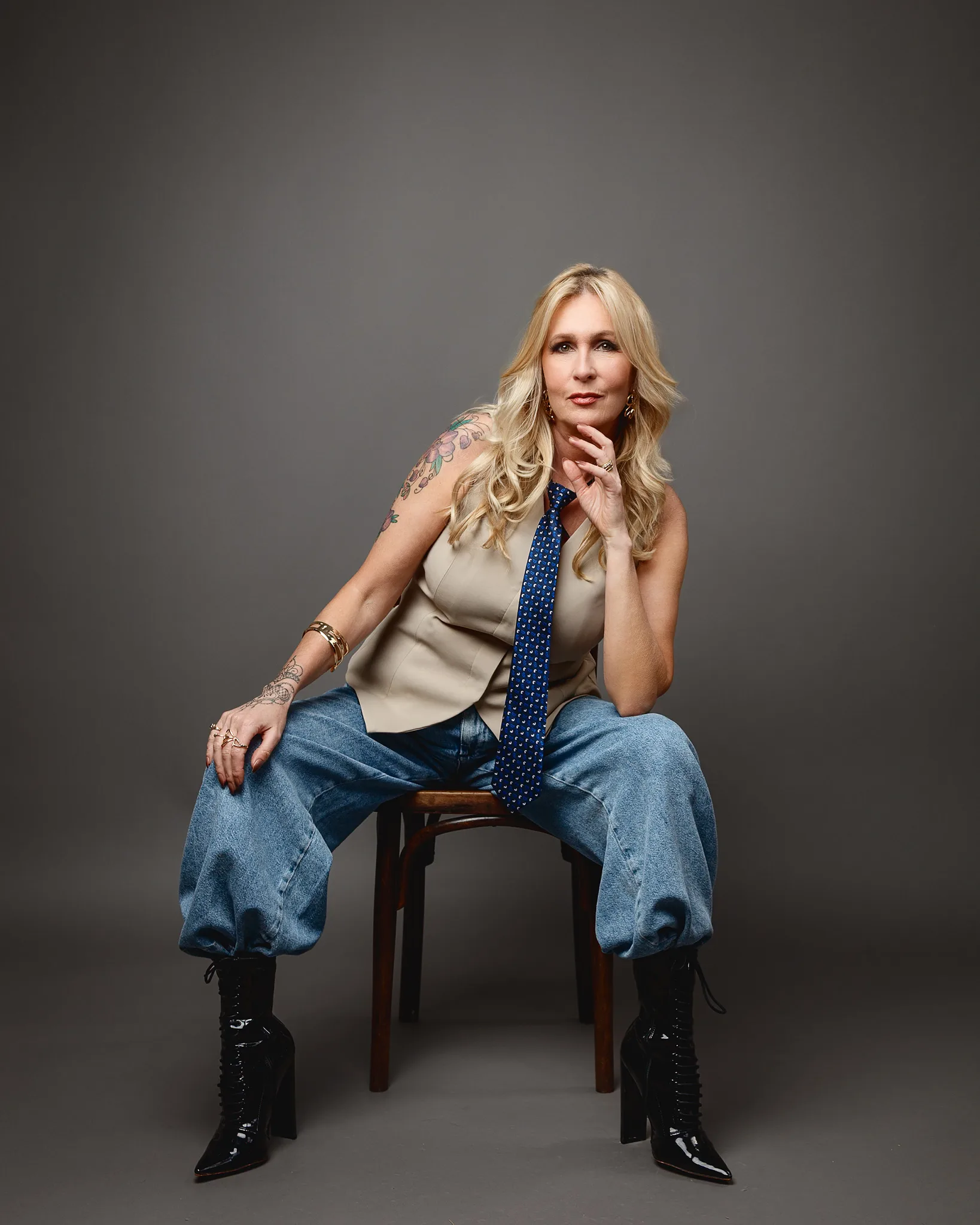 Woman in tie and jeans seated on stool