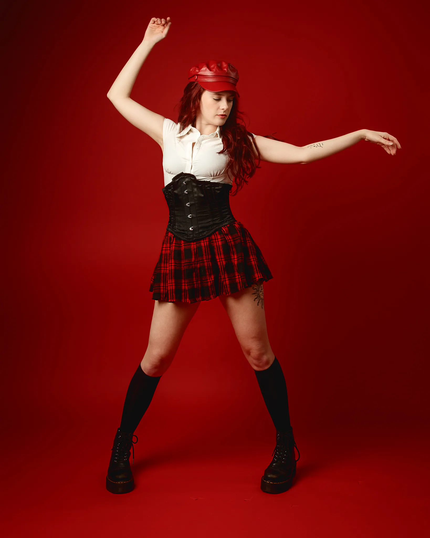 Woman in tartan skirt posing against red background
