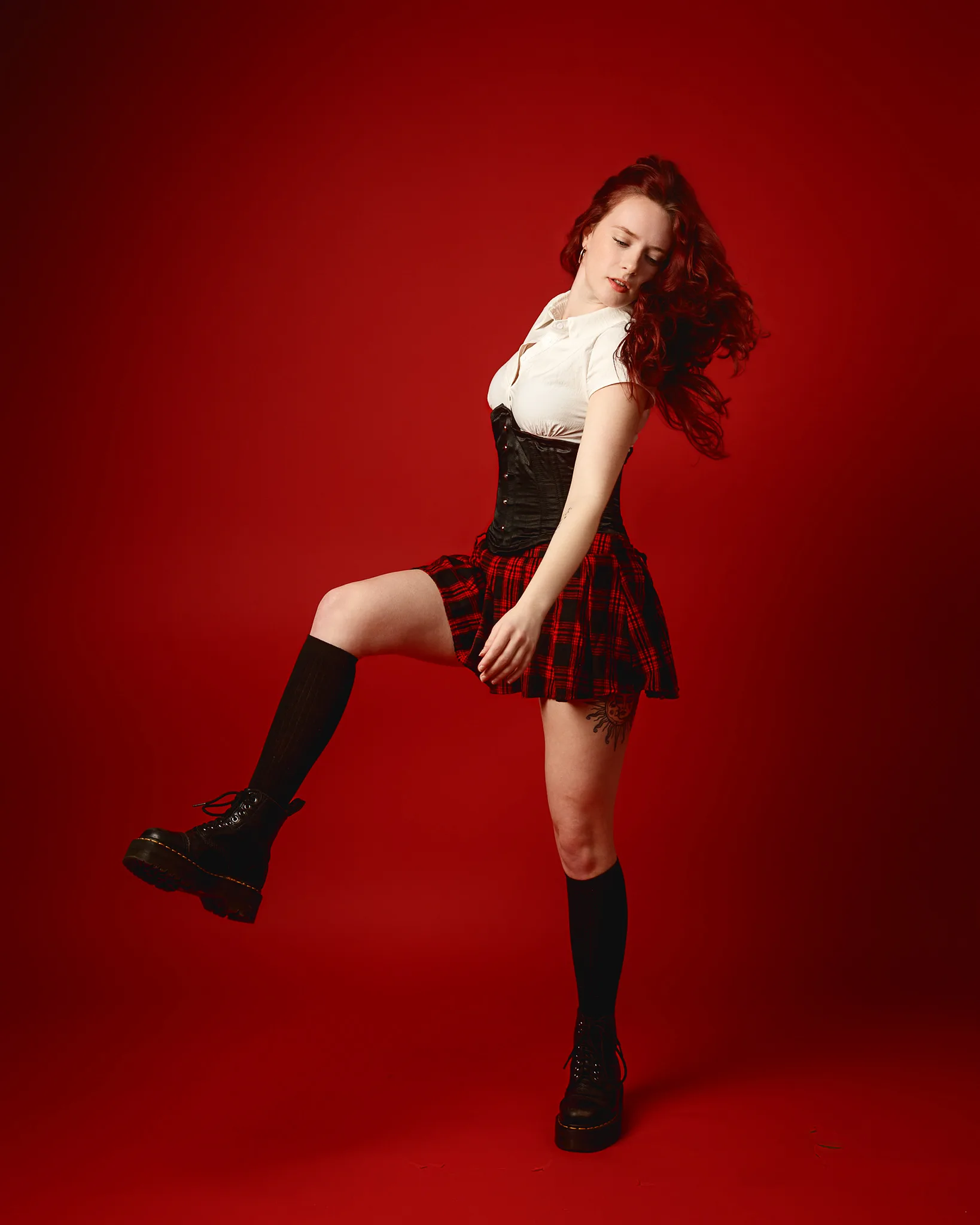 Woman posing in tartan skirt against red backdrop