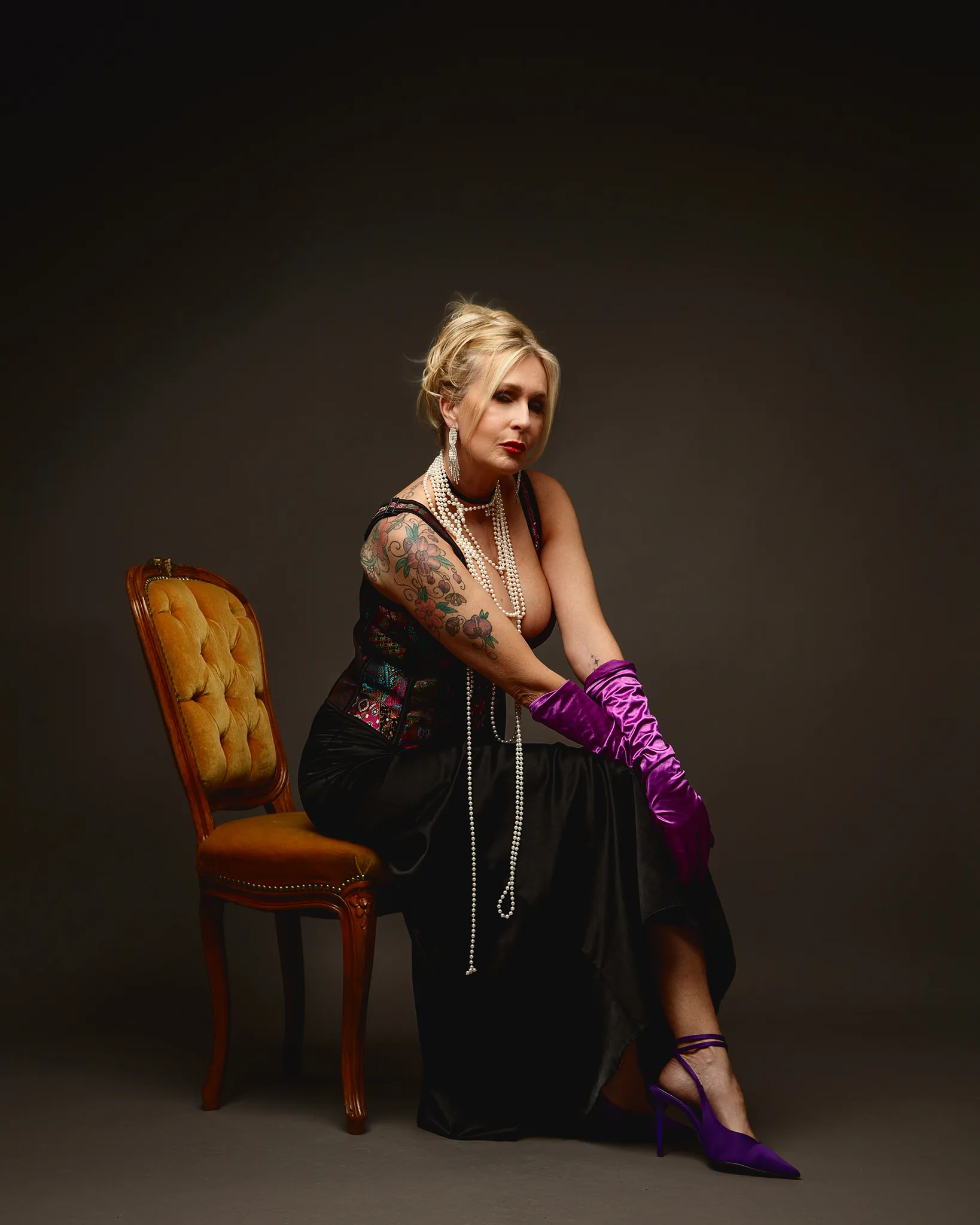 Glamorous woman in pearls and purple gloves seated