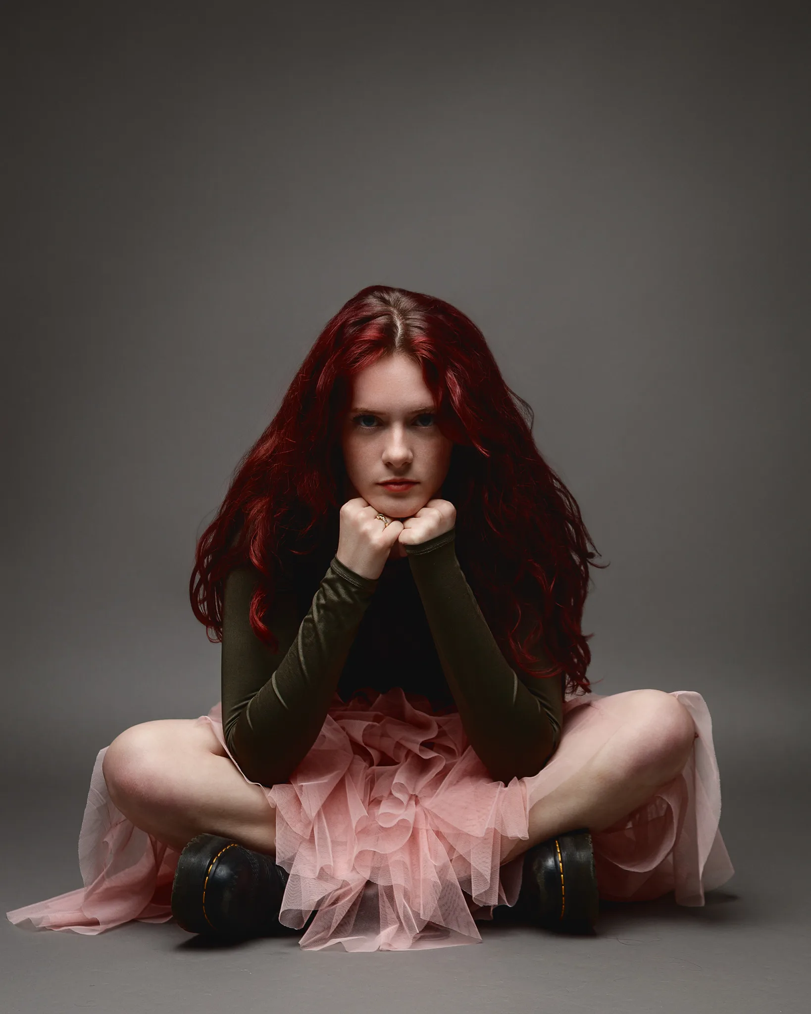 Red-haired woman sitting cross-legged in studio portrait
