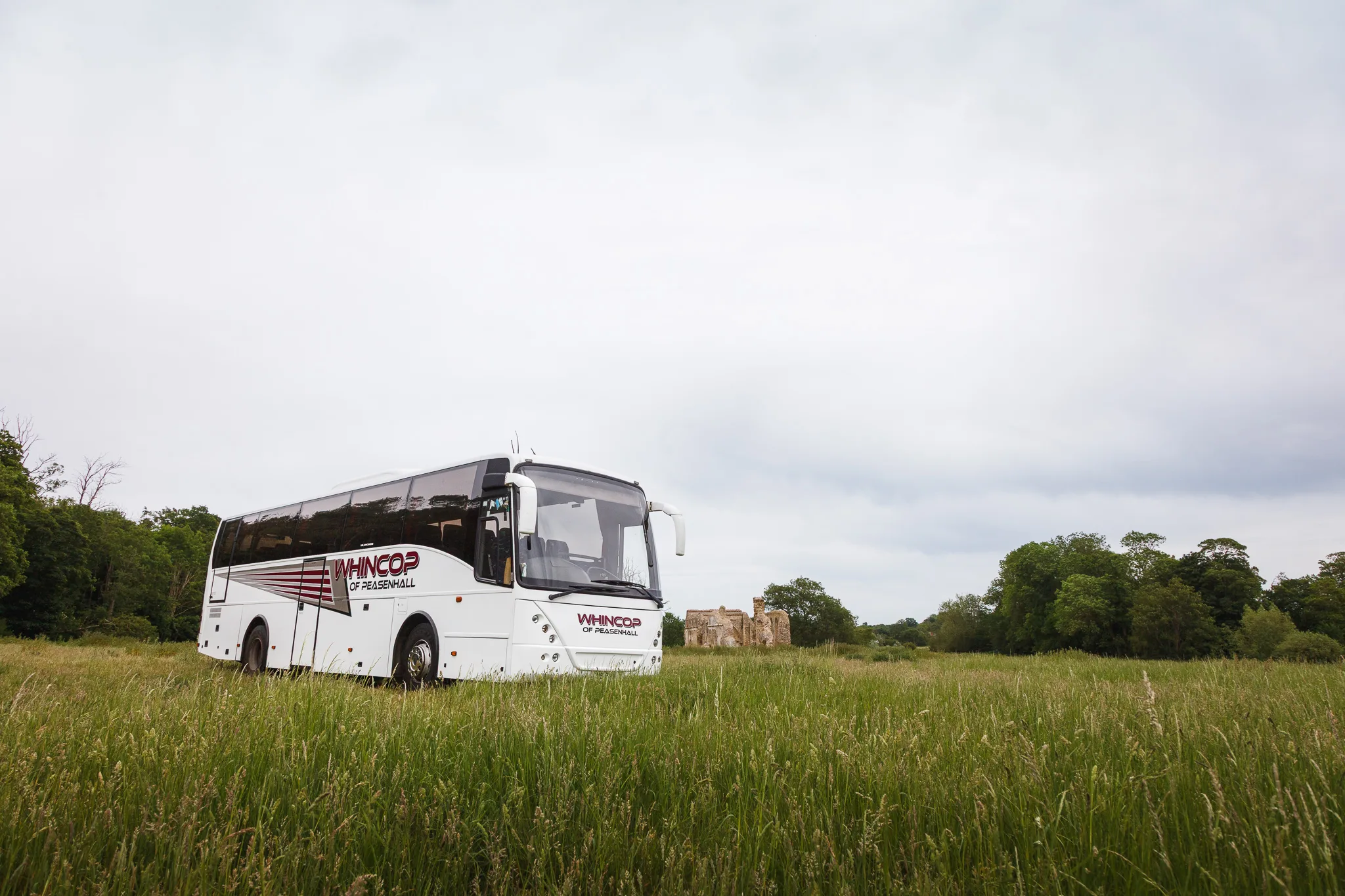 White coach in grassy field near ruins