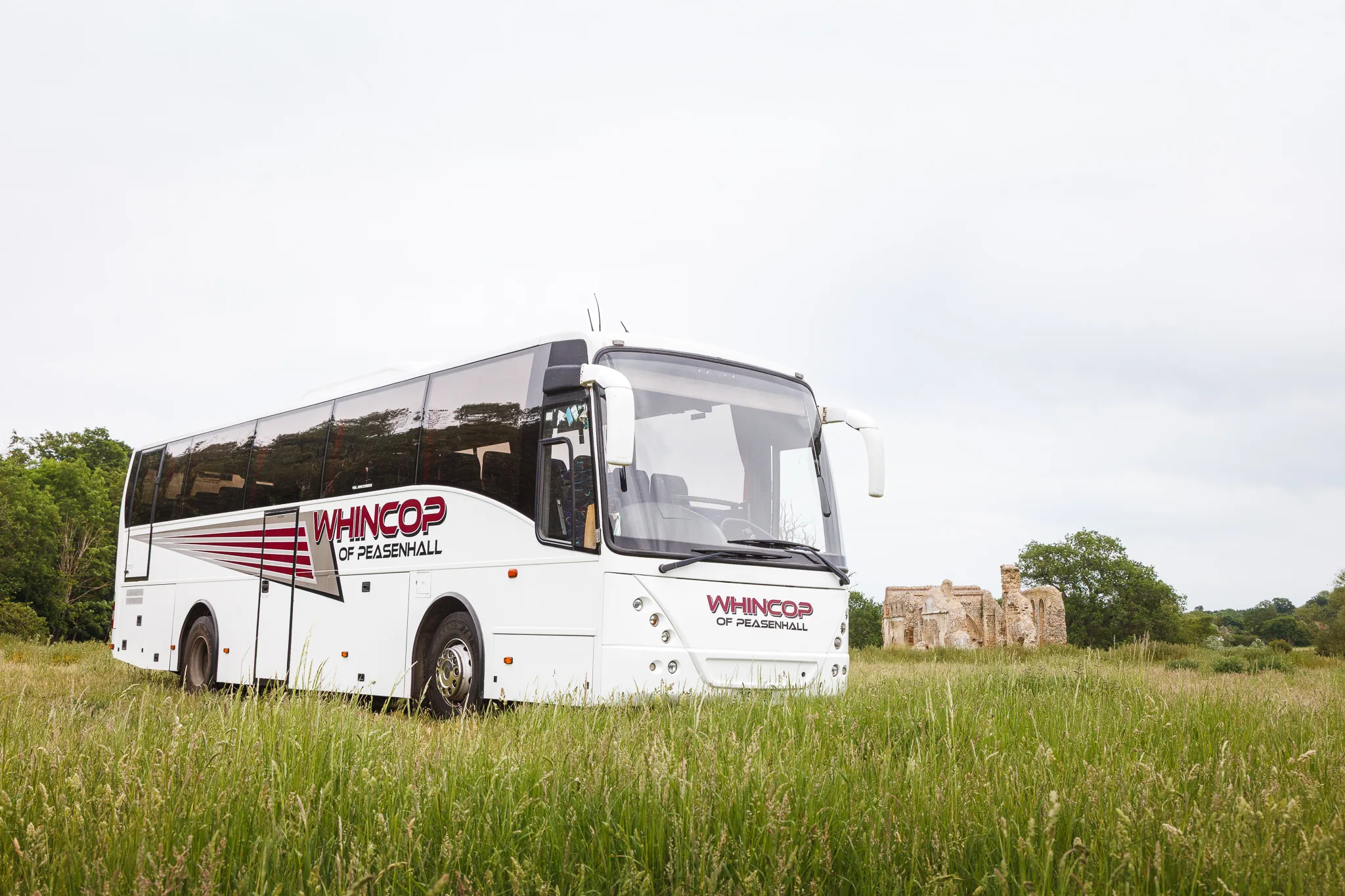 White coach in grassy field near historic ruins