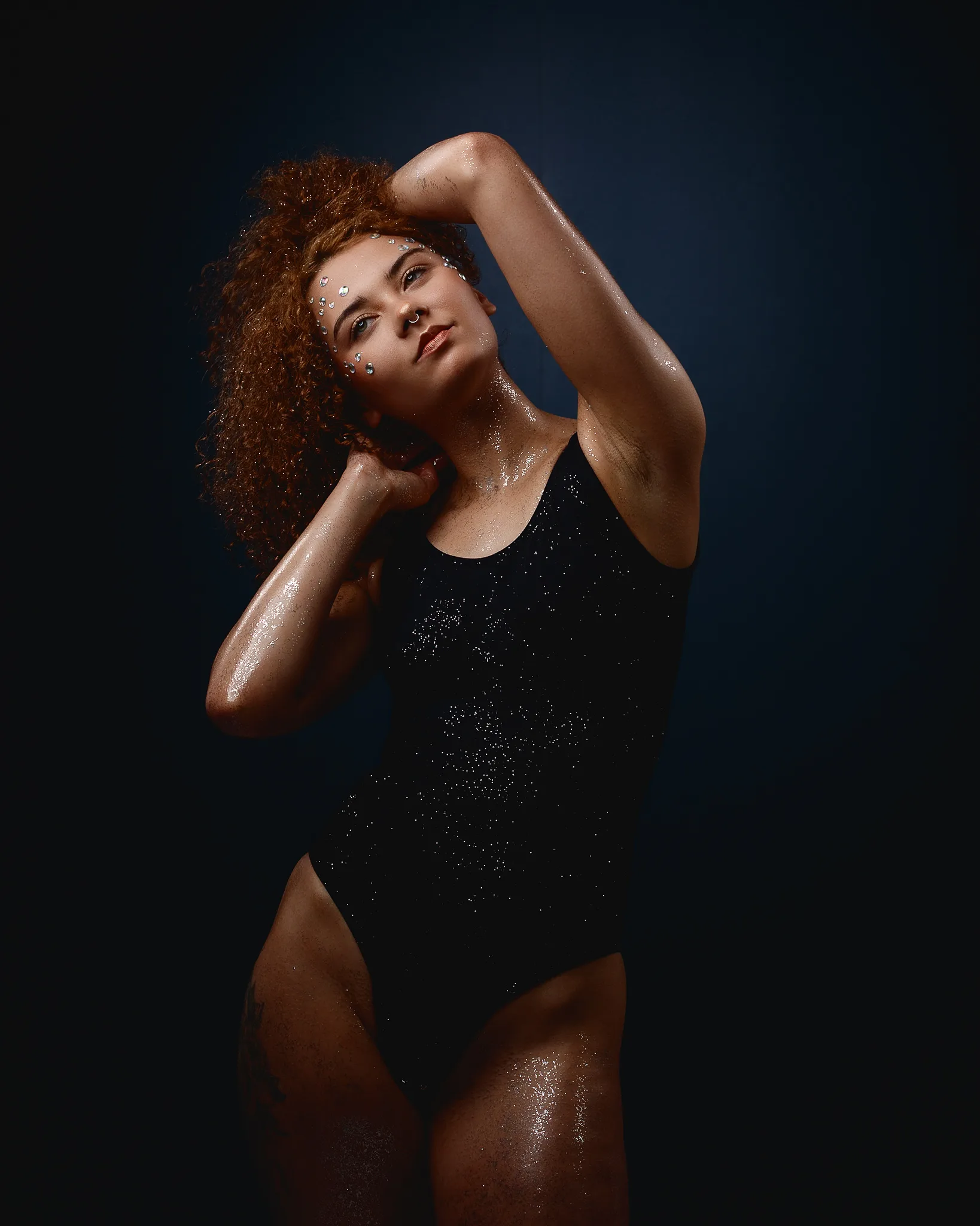 Woman with curly red hair wearing sparkly black top, posed against dark background