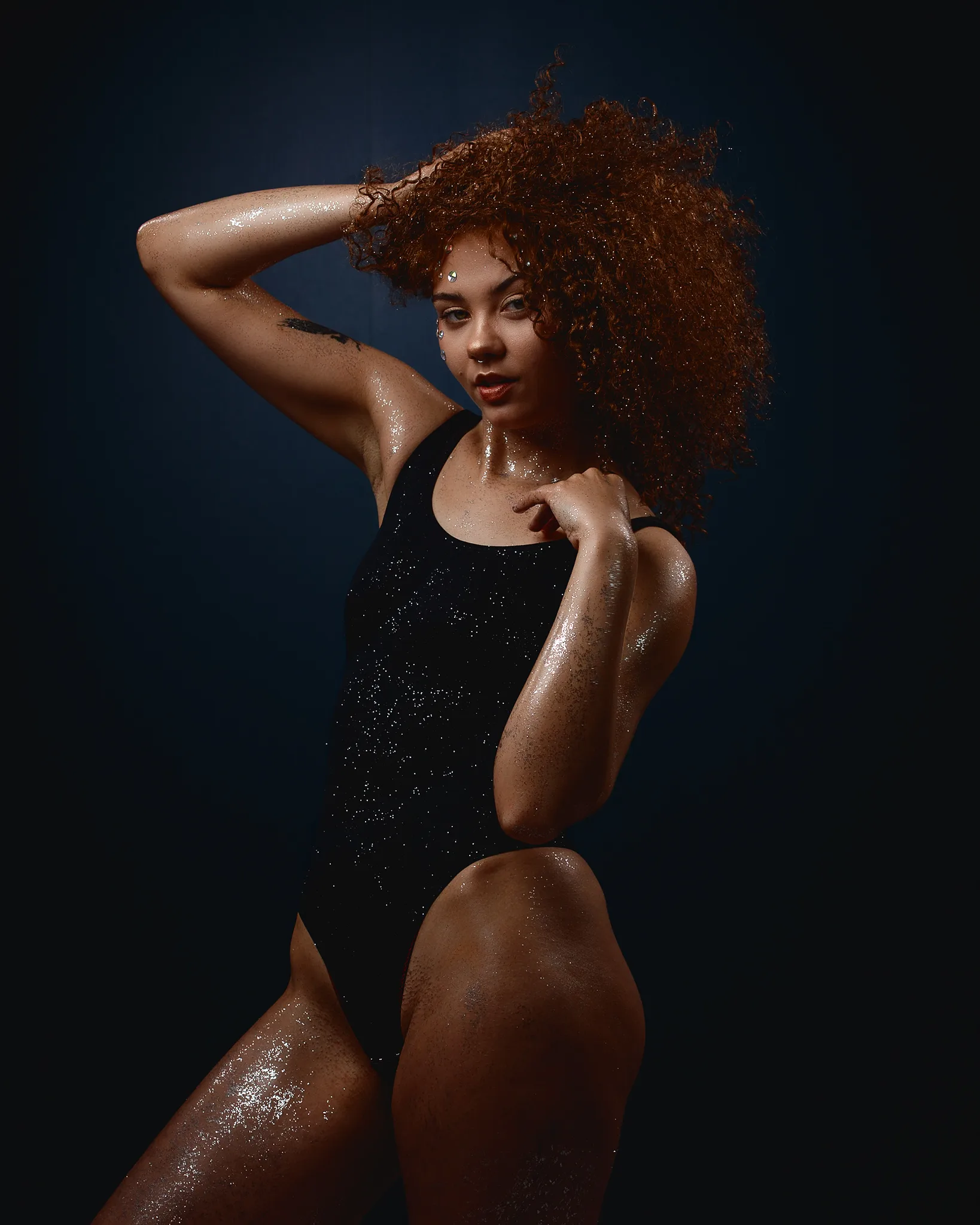Woman with curly reddish-brown hair posing against dark blue background