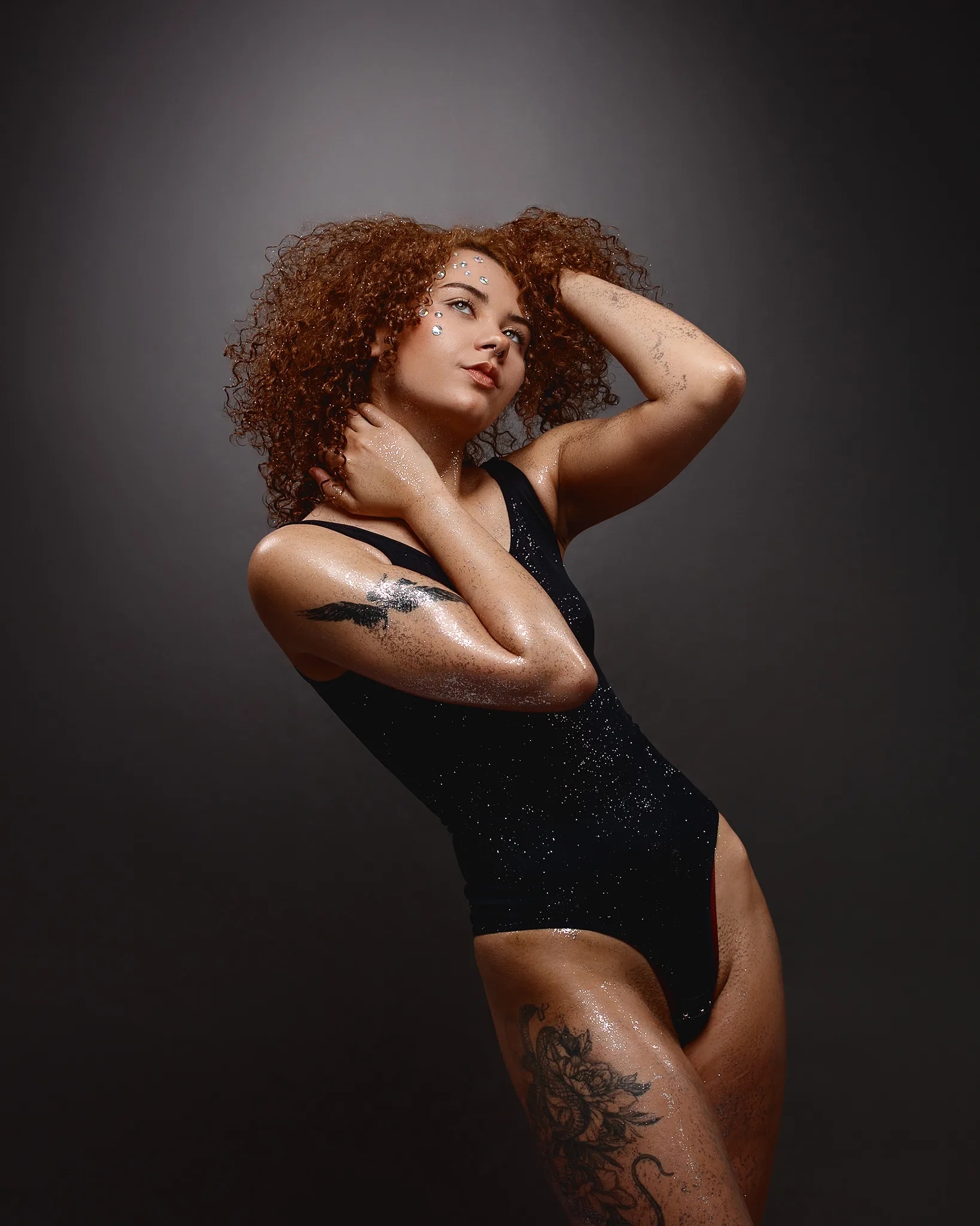 Woman with curly red hair wearing sparkly black swimsuit posing