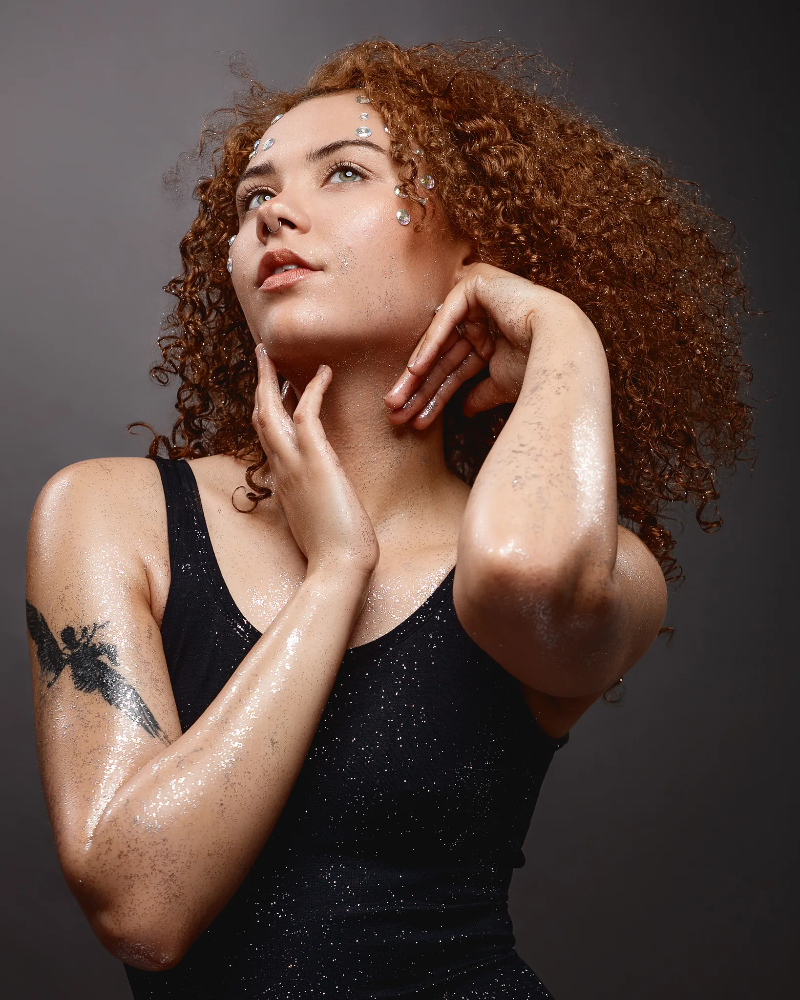 Woman with curly auburn hair and glitter makeup looking upward