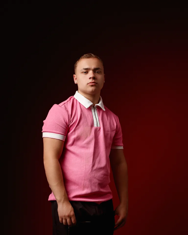 Young man wearing pink polo shirt against dark background