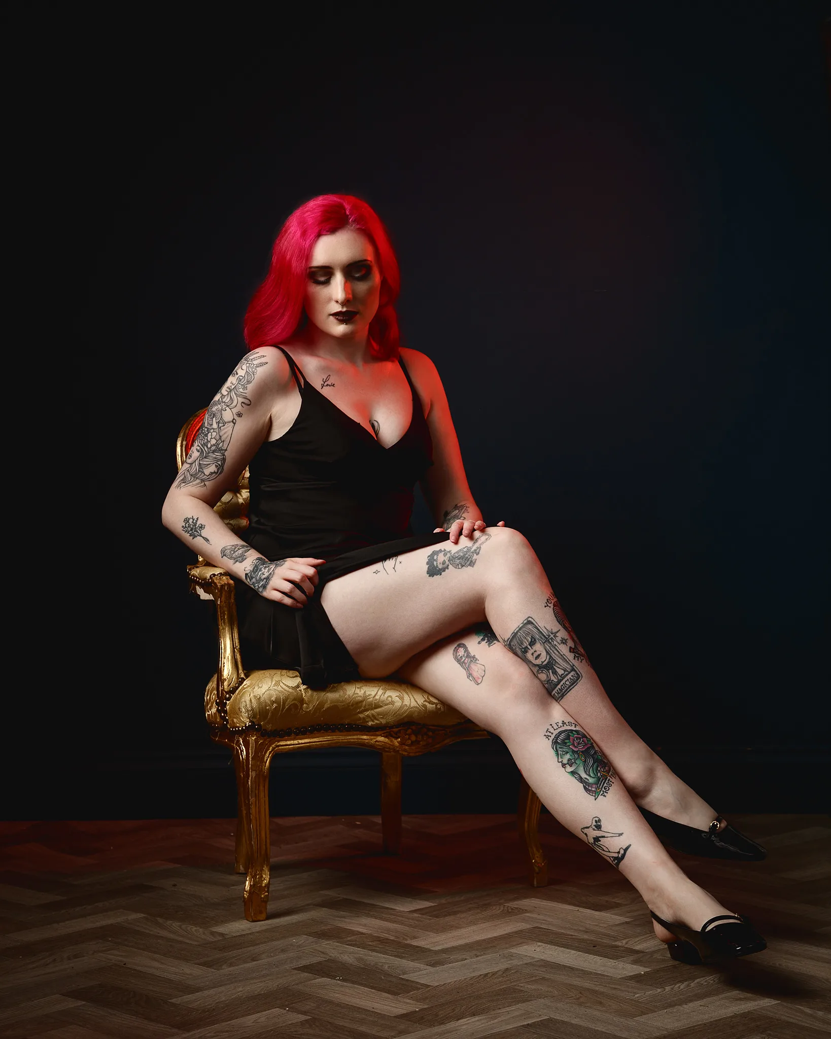 Woman with bright red hair and tattoos sitting on gold chair