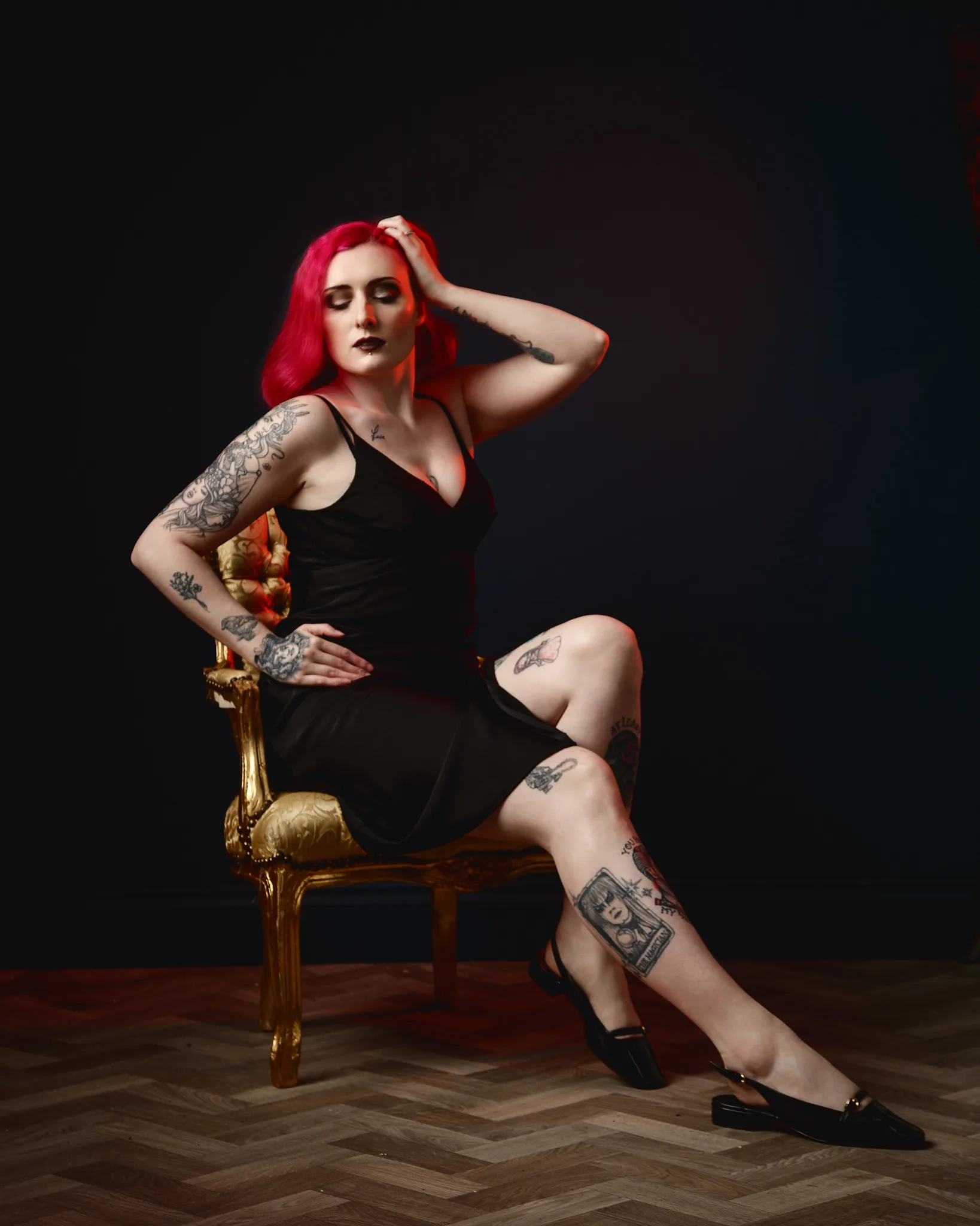 Woman with vibrant red hair and tattoos seated on ornate gold chair