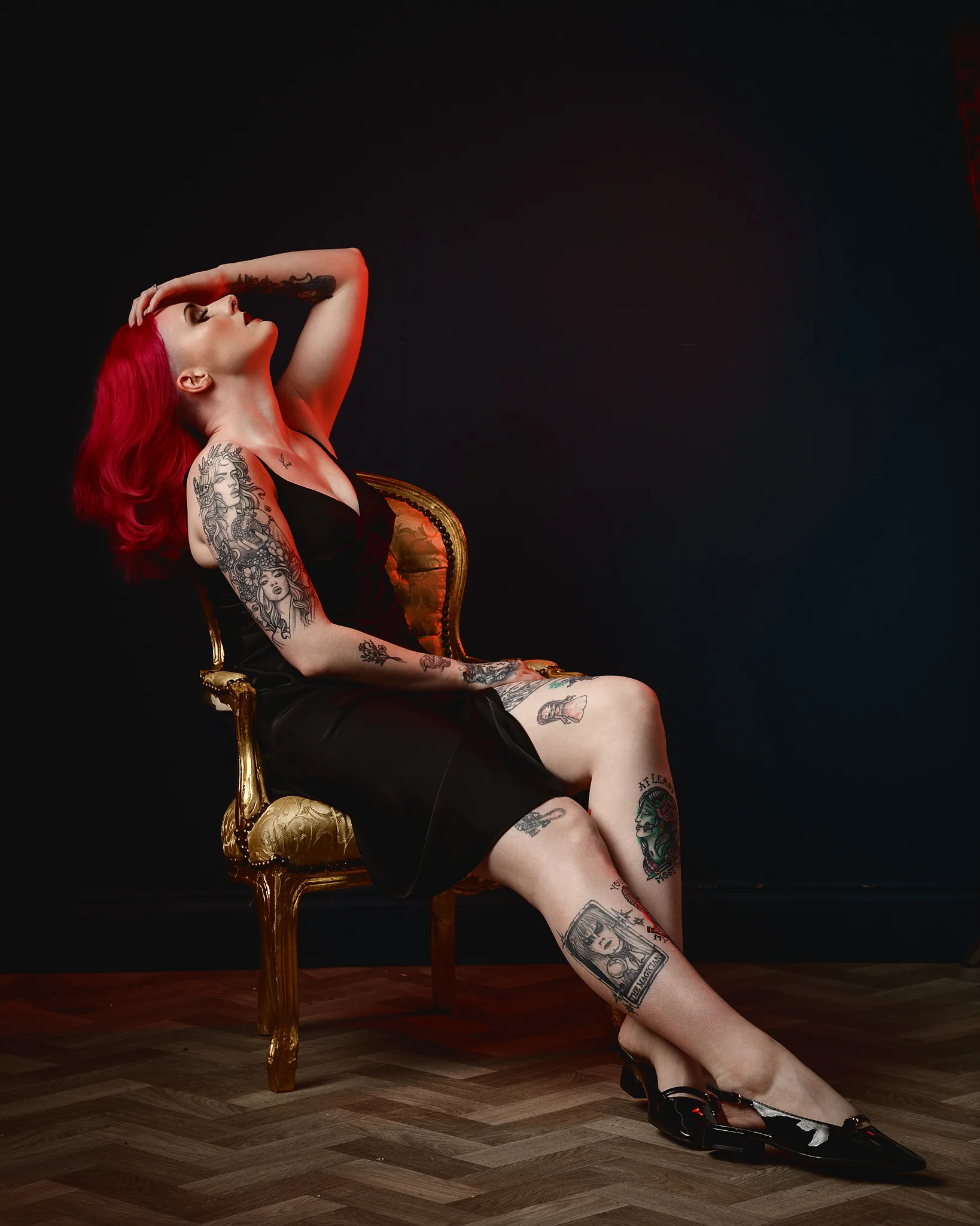 Woman with red hair and tattoos sitting on ornate gold chair