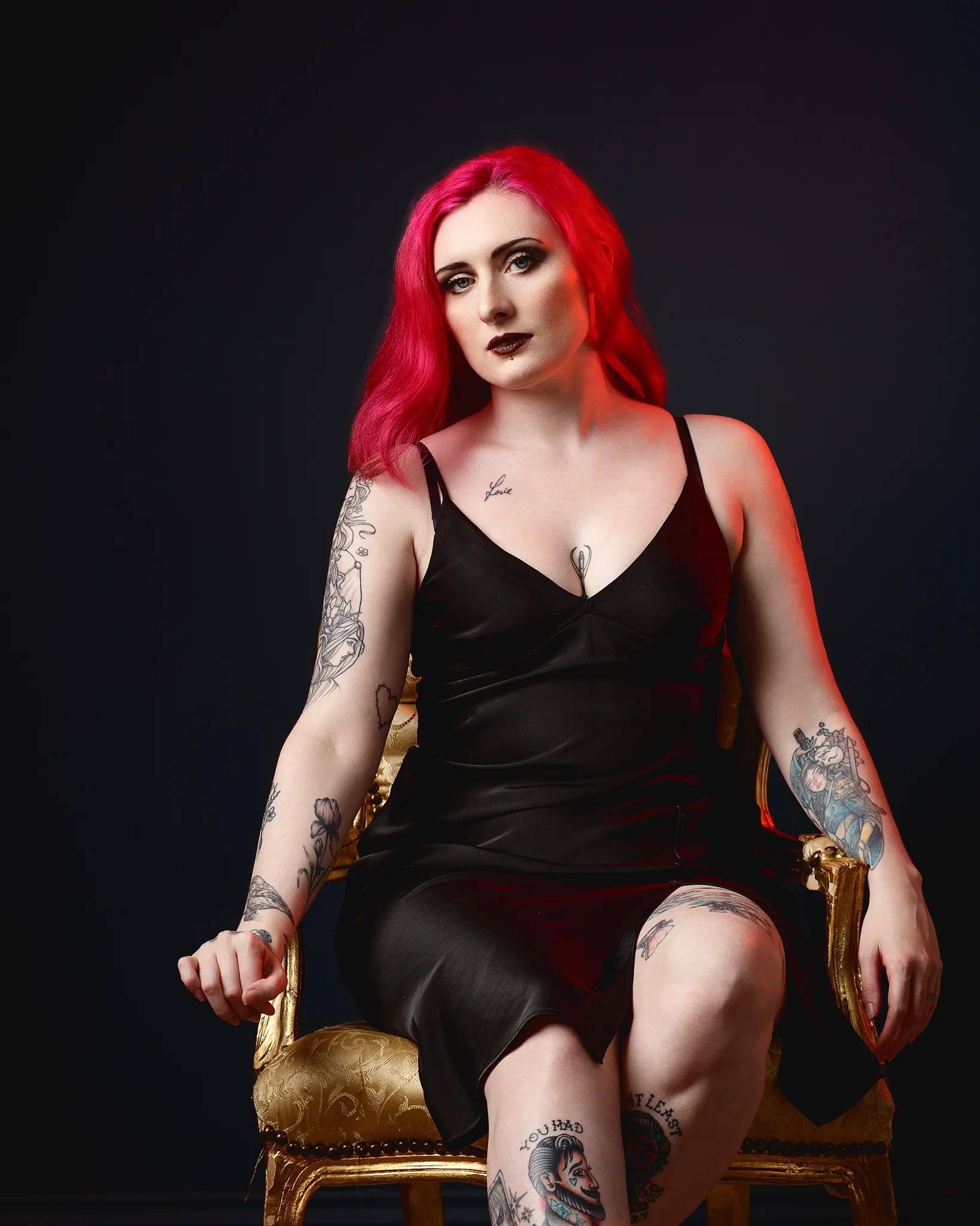 Woman with vibrant red hair and multiple tattoos seated on ornate chair