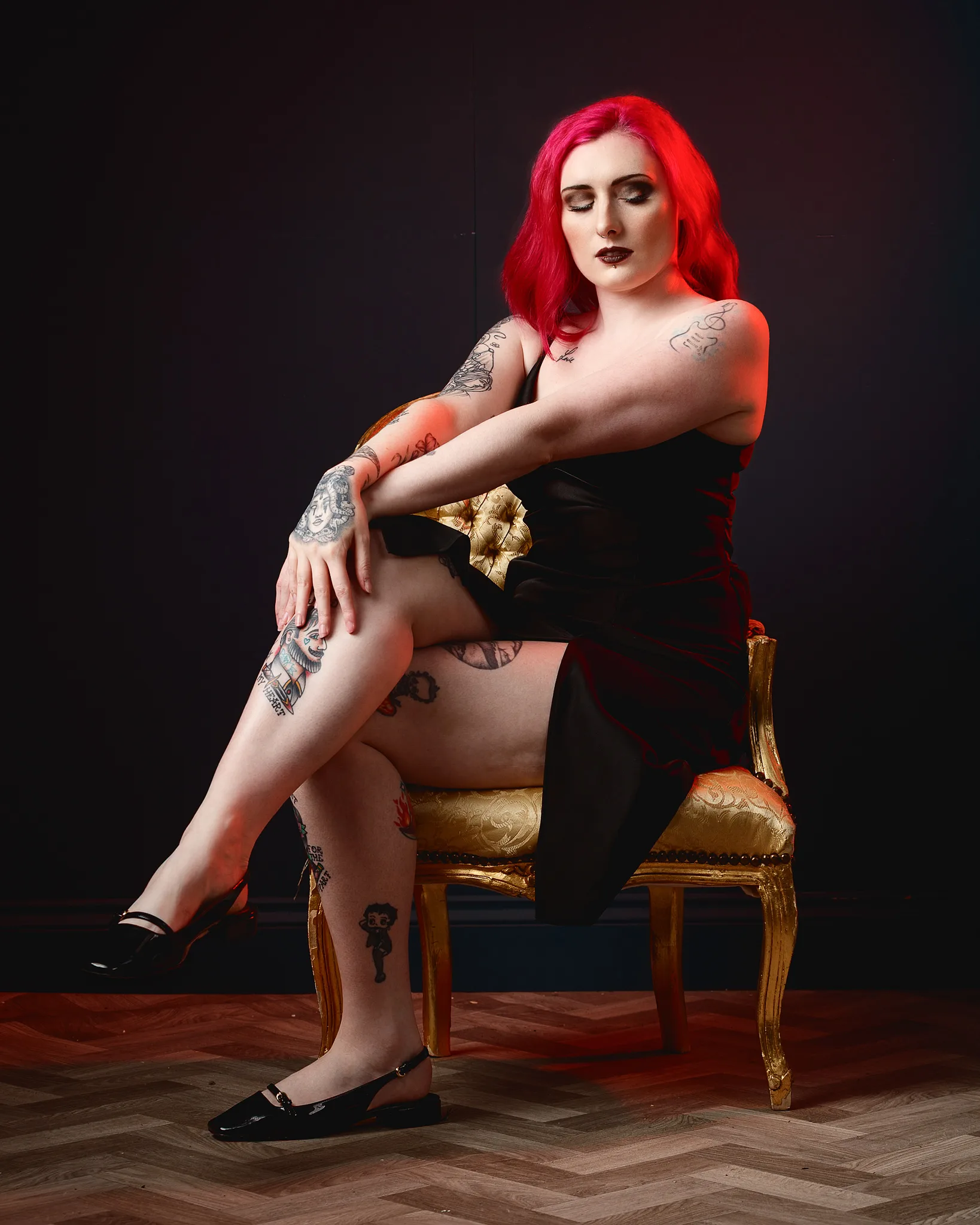 Woman with vibrant red hair and tattoos seated on ornate gold chair