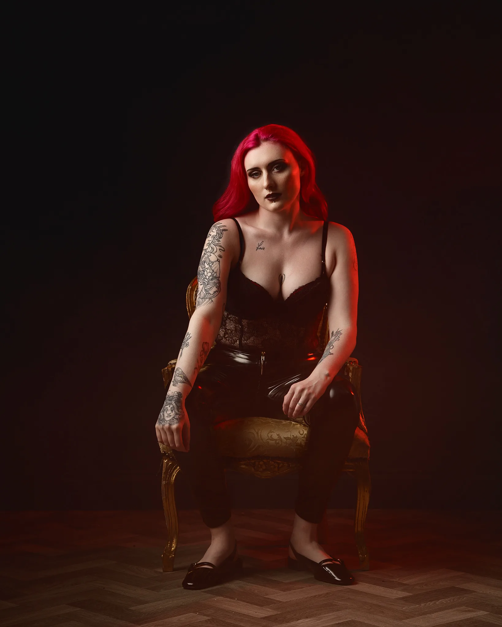 Woman with vibrant red hair and tattoos seated on ornate chair