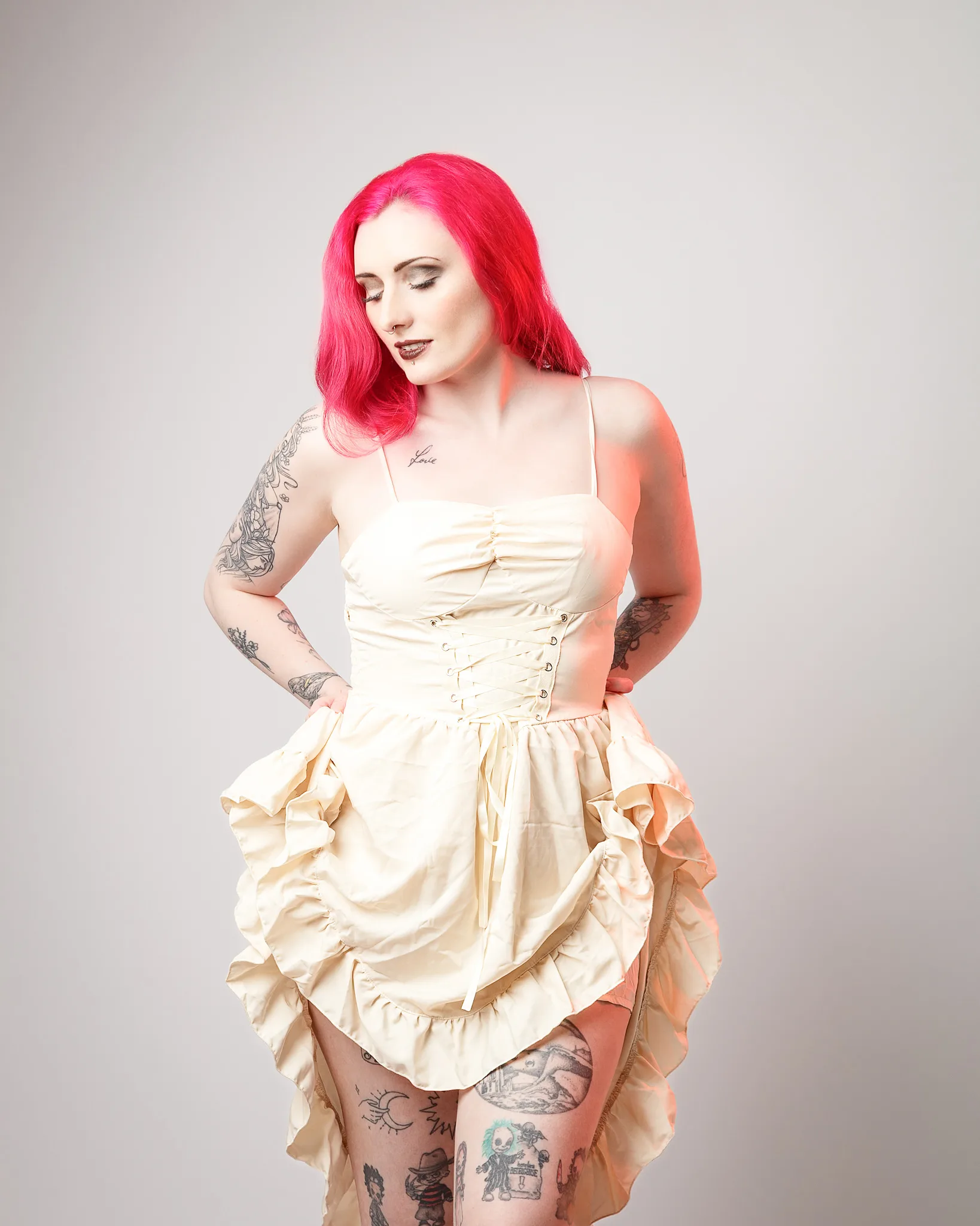 Woman with pink hair wearing cream corset dress with tattoos