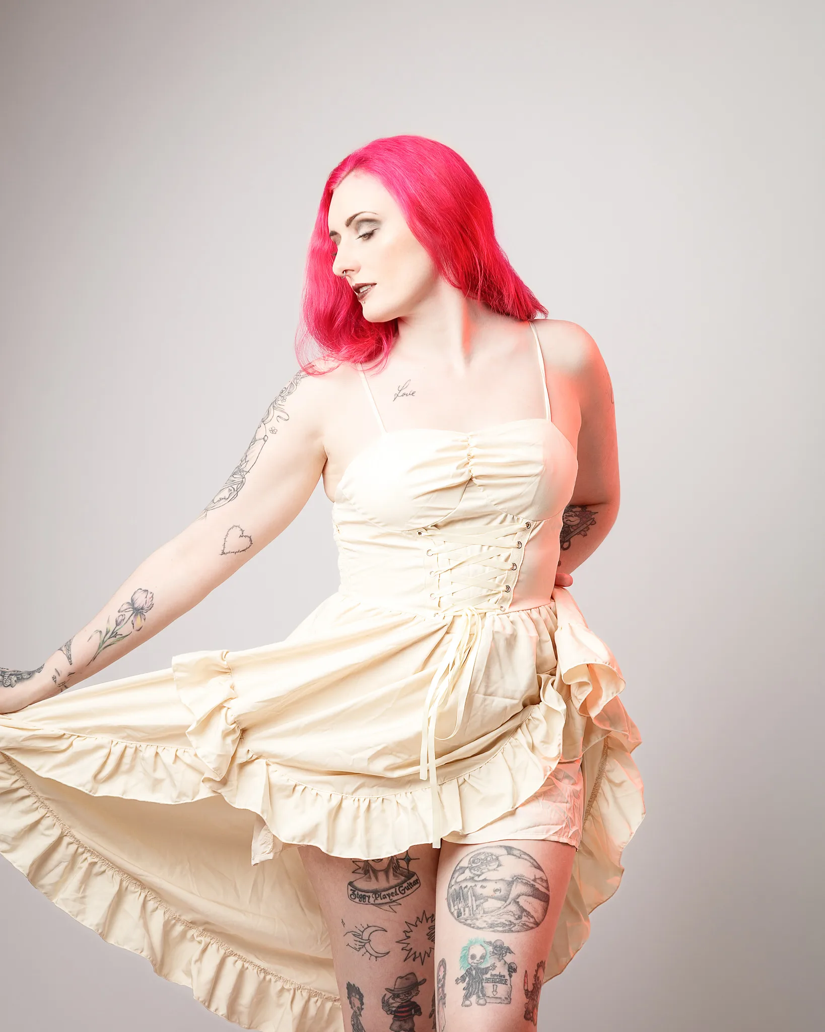 Woman with bright pink hair wearing cream dress with tattoos
