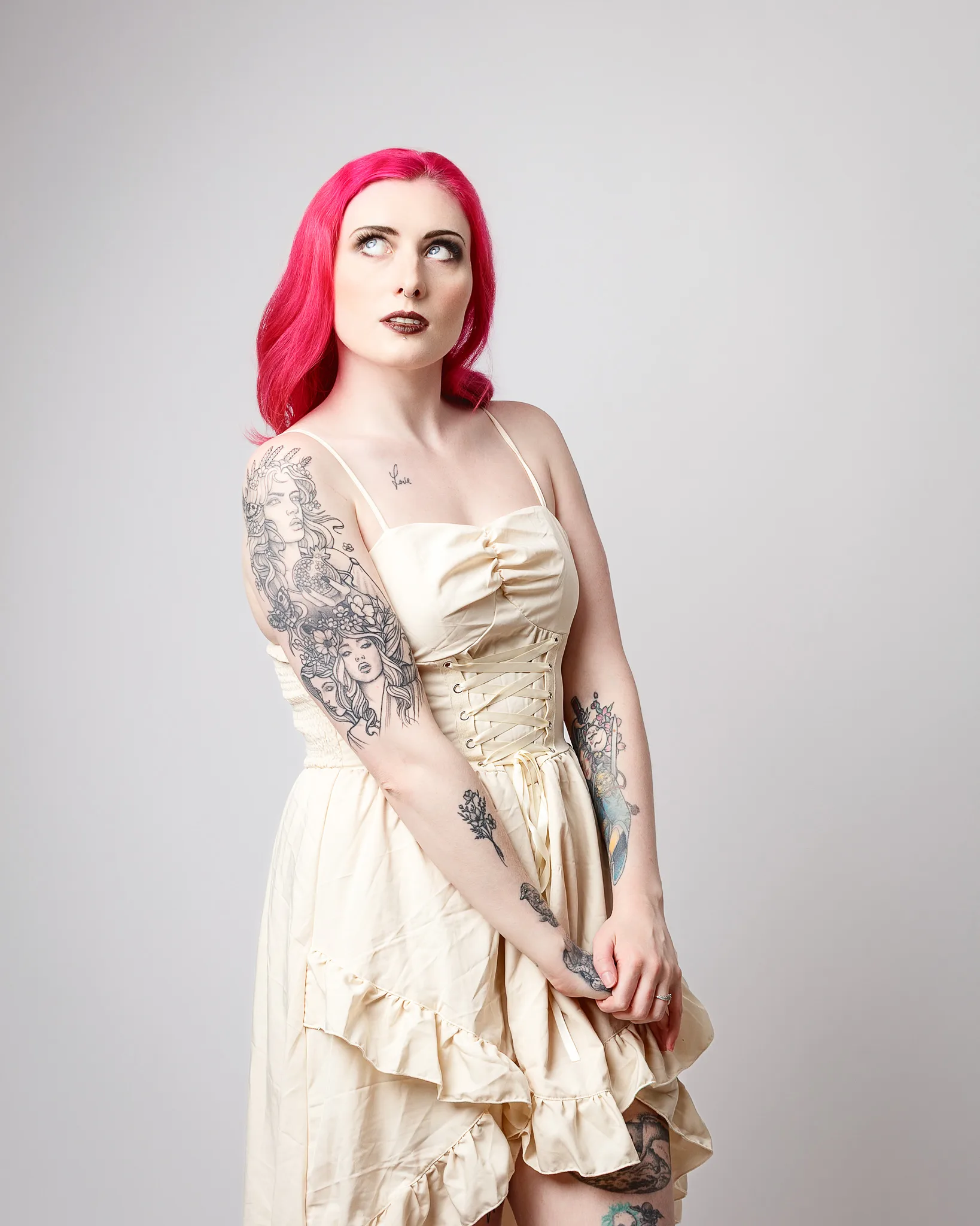 Woman with bright pink hair wearing cream corset dress with tattoos