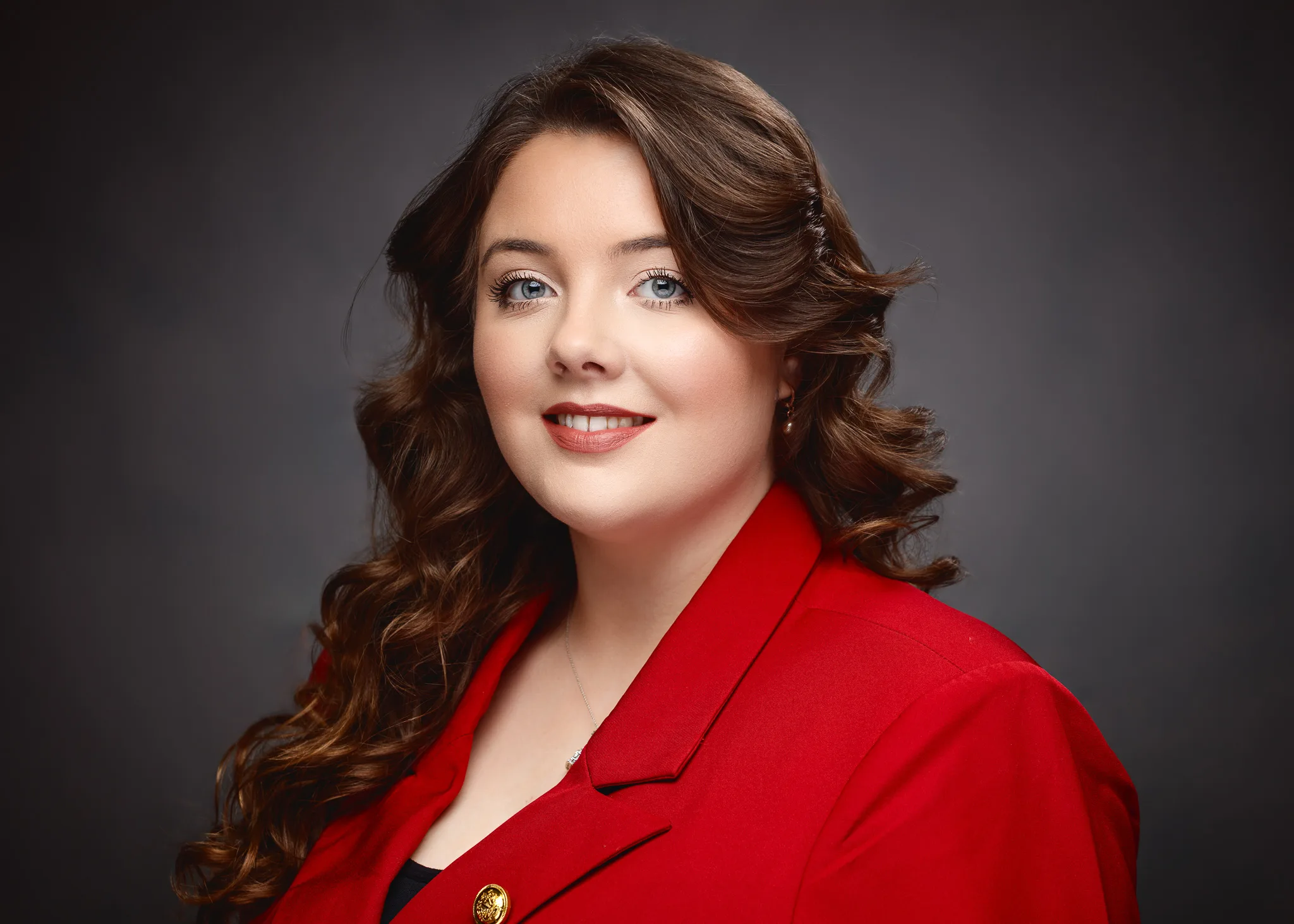 Woman with brown wavy hair wearing red blazer smiling