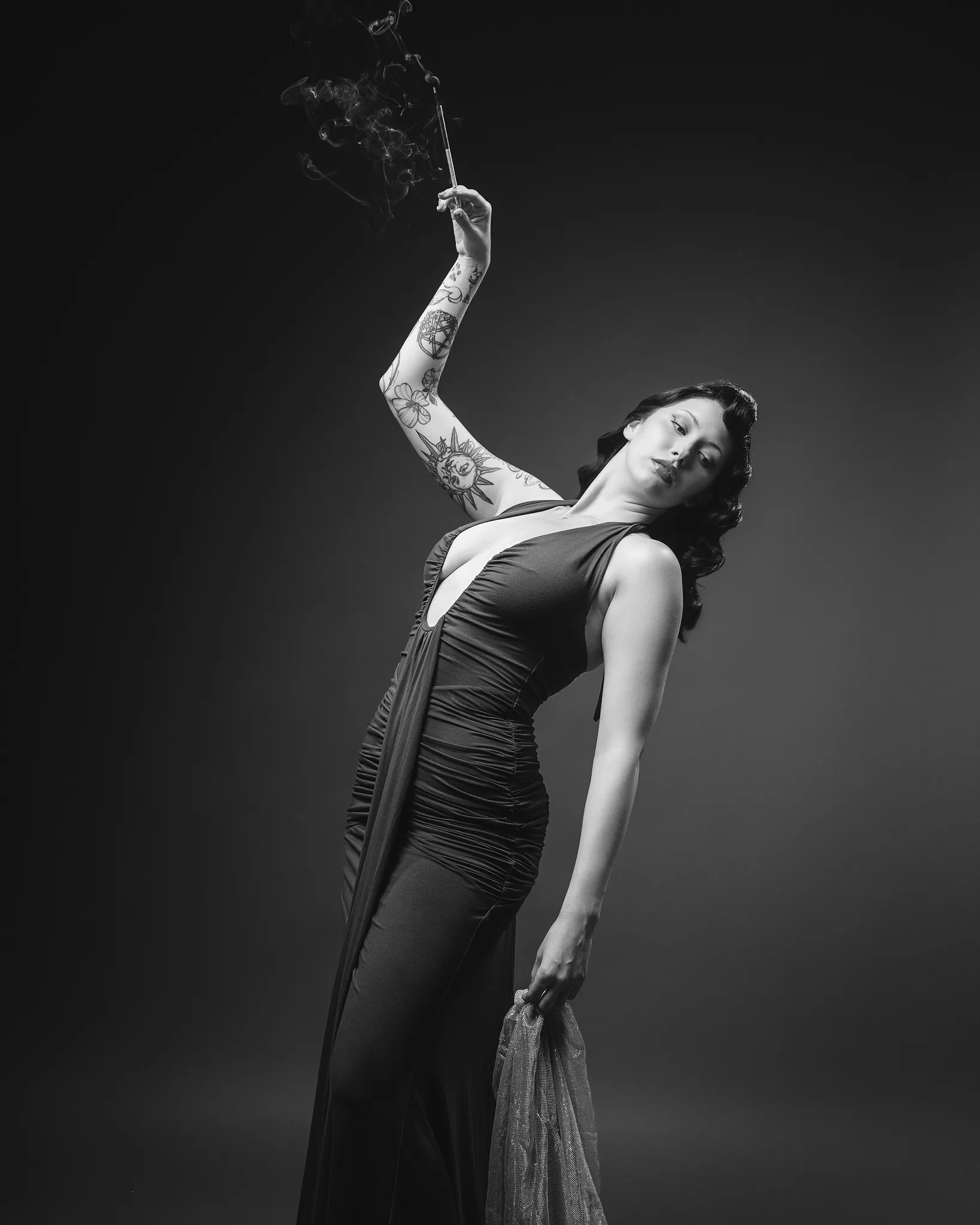 Tattooed woman in elegant dress holding smoking cigarette holder