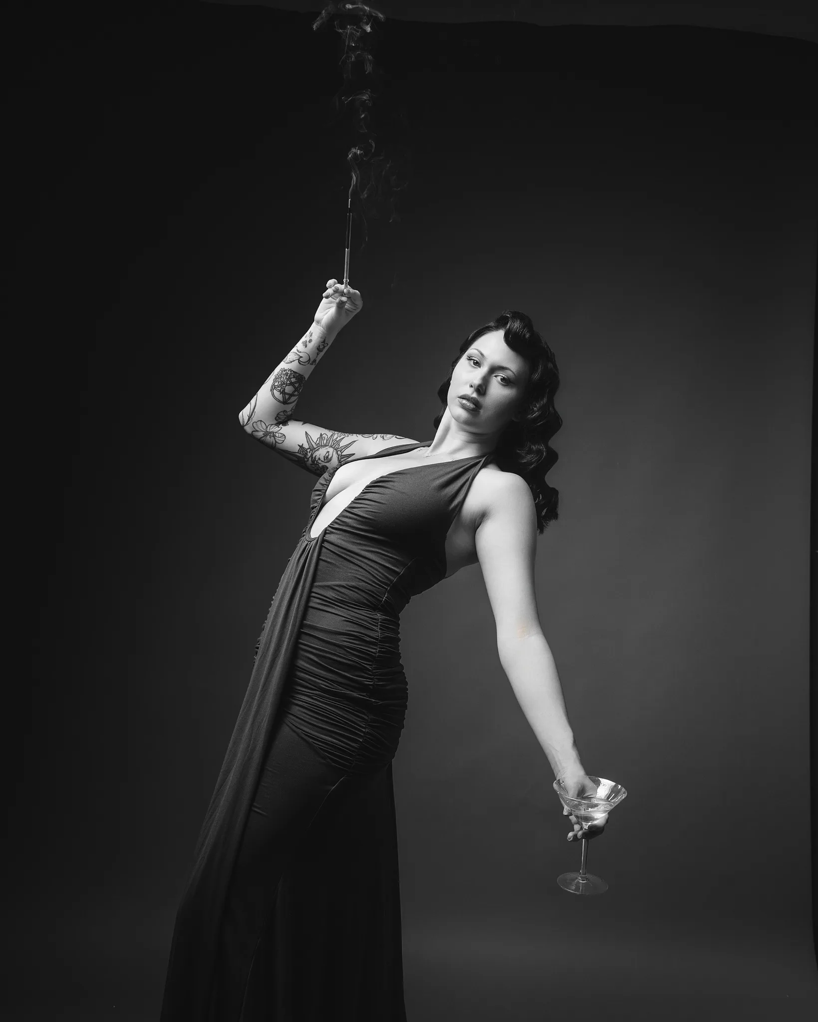 Tattooed woman in black dress holding cocktail and rose
