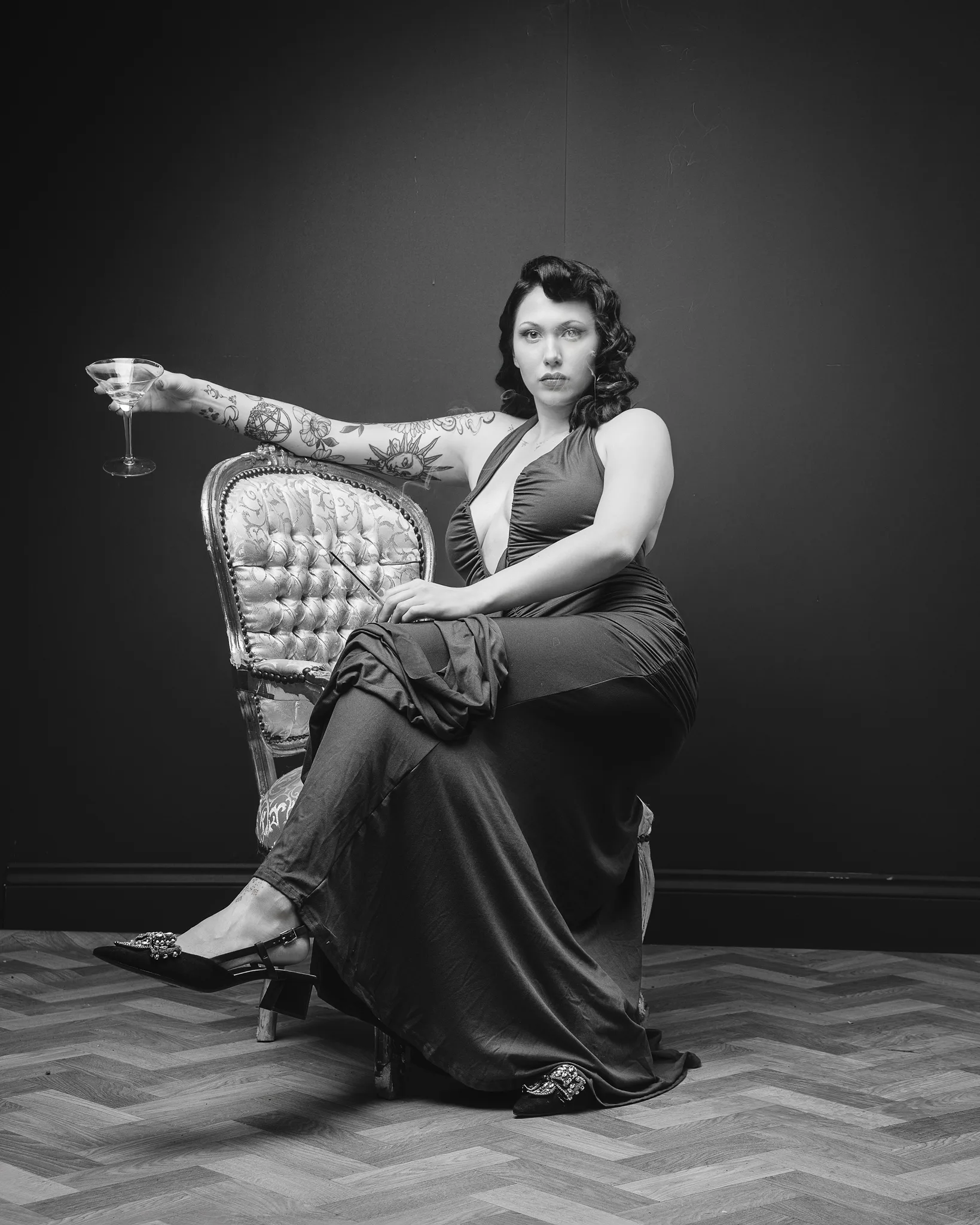 Tattooed woman seated on ornate chair holding martini glass