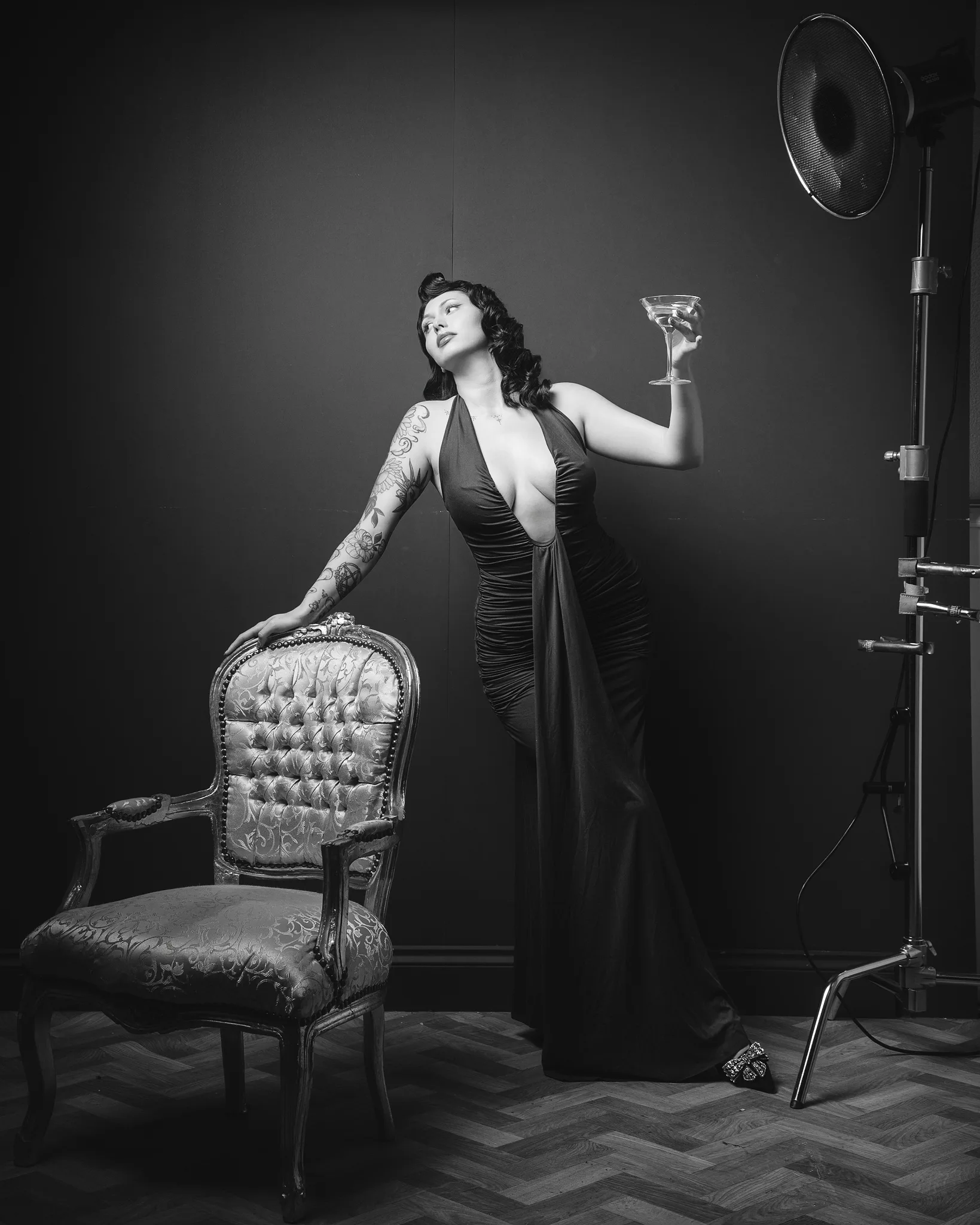 Woman in black dress holding cocktail beside ornate chair