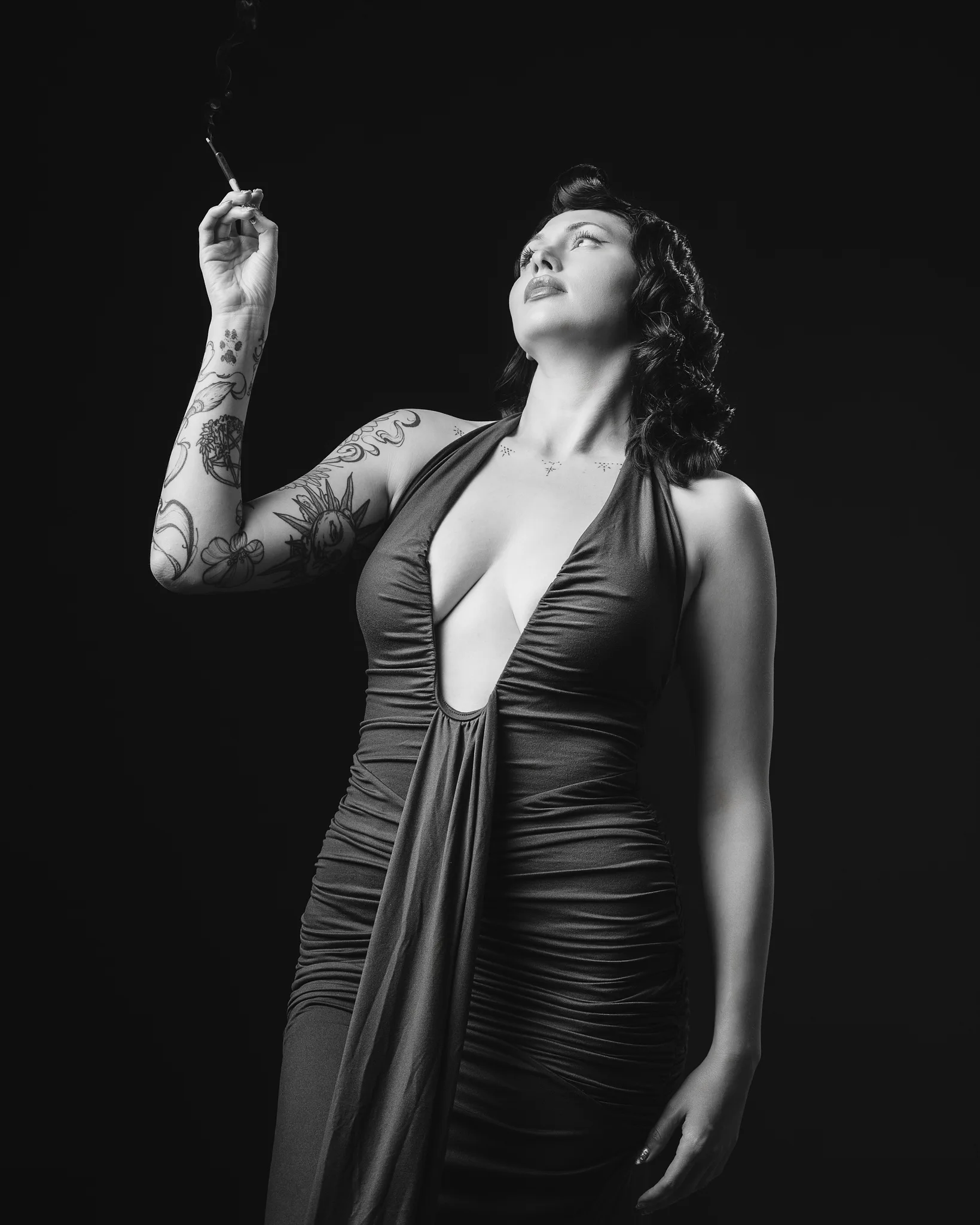 Tattooed woman in draped dress holding cigarette upward
