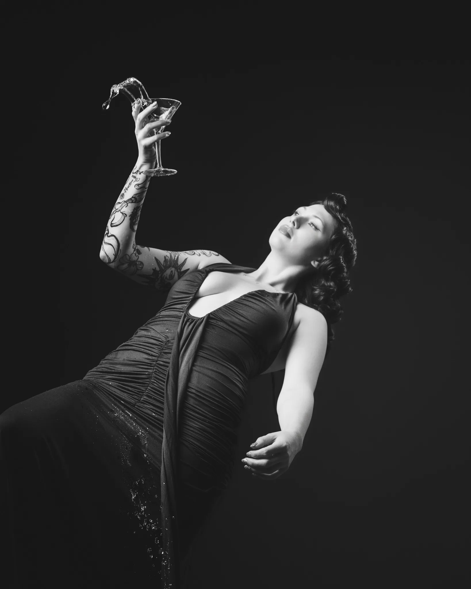 Tattooed woman in black dress holding cocktail glass
