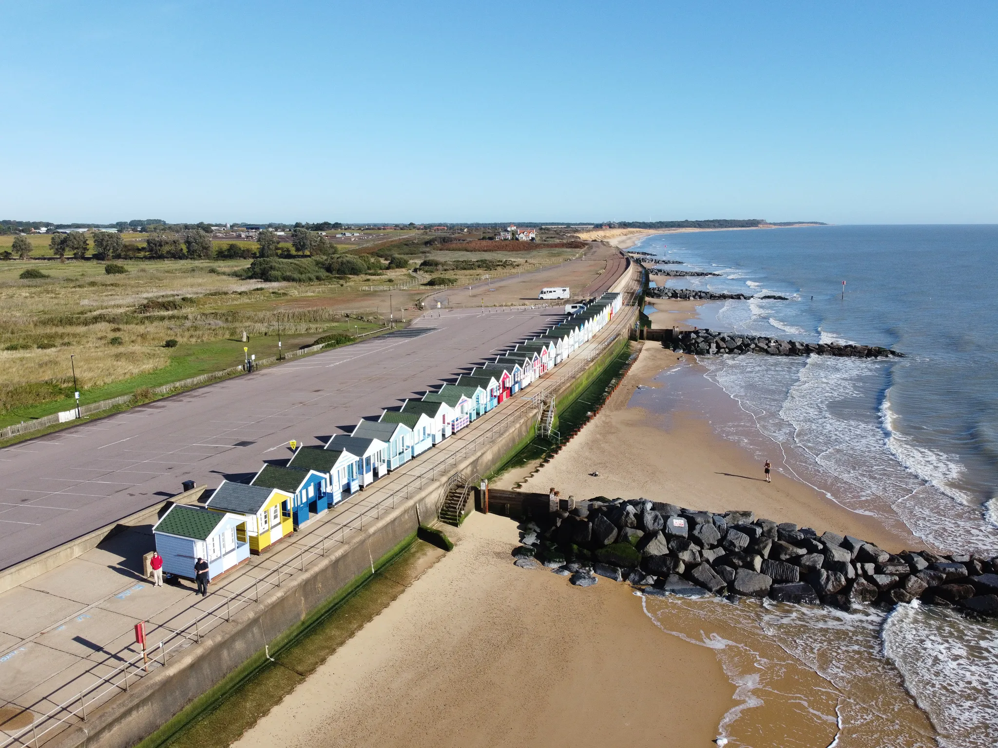 Colourful beach huts line sandy seaside promenade with waves