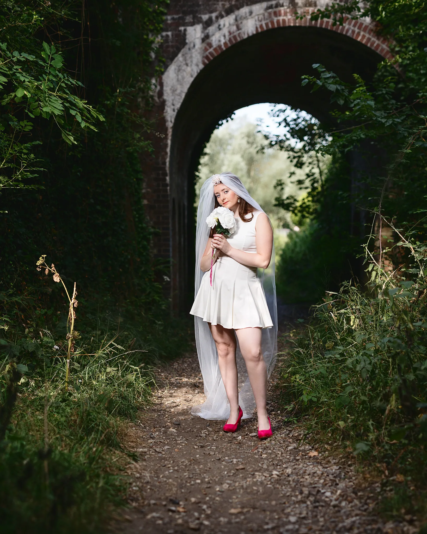 Bride in white dress under brick railway arch