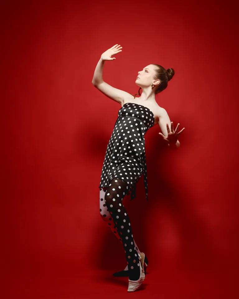 Woman in polka dot dress posing against red background