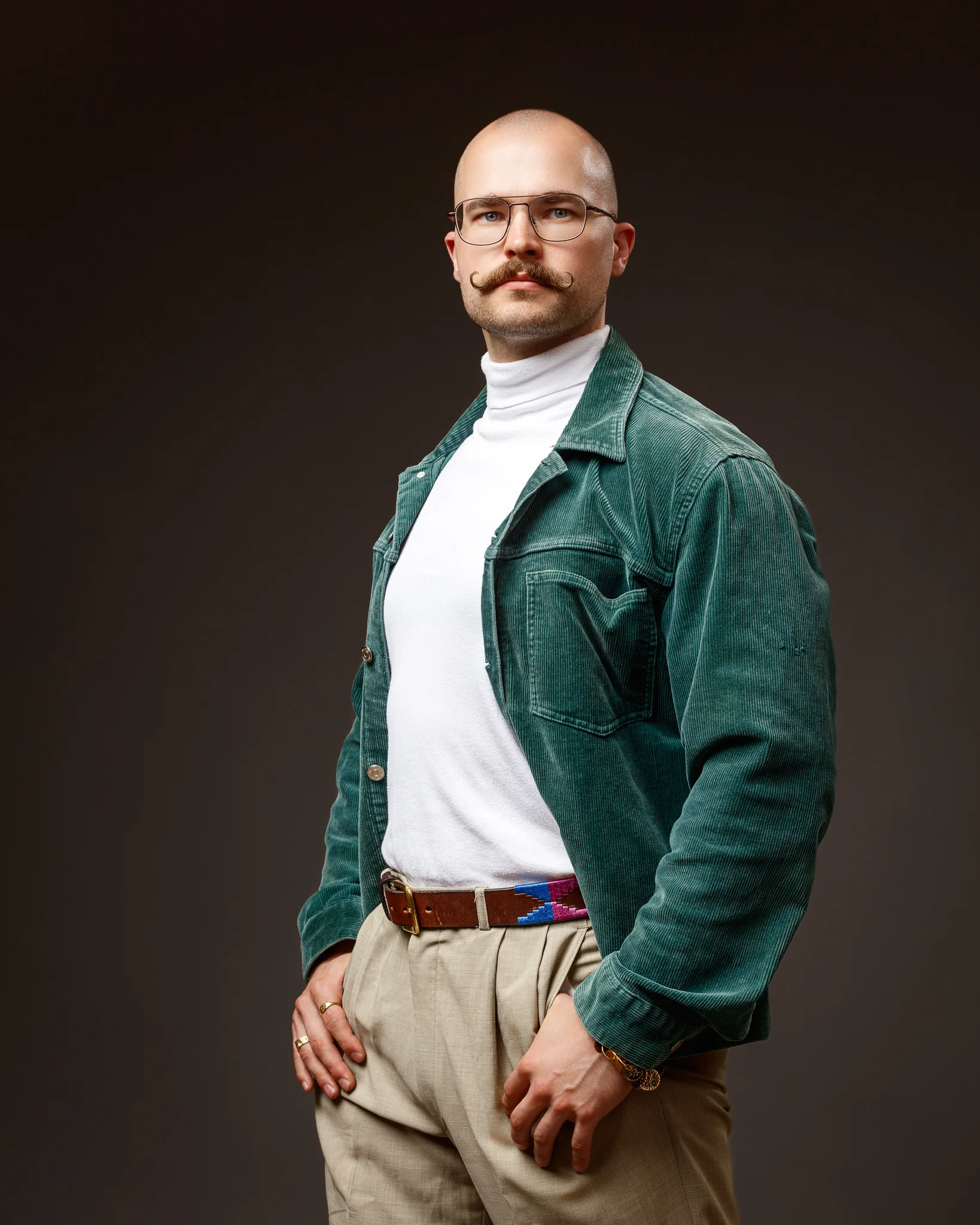 Man wearing green corduroy jacket and glasses against dark background