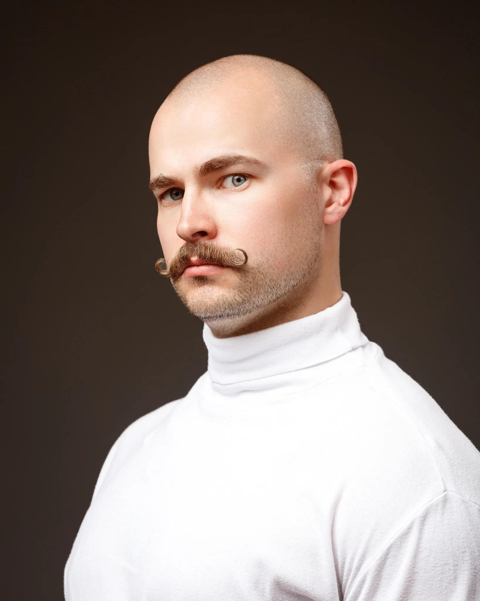 Bald man with curled moustache wearing white turtleneck
