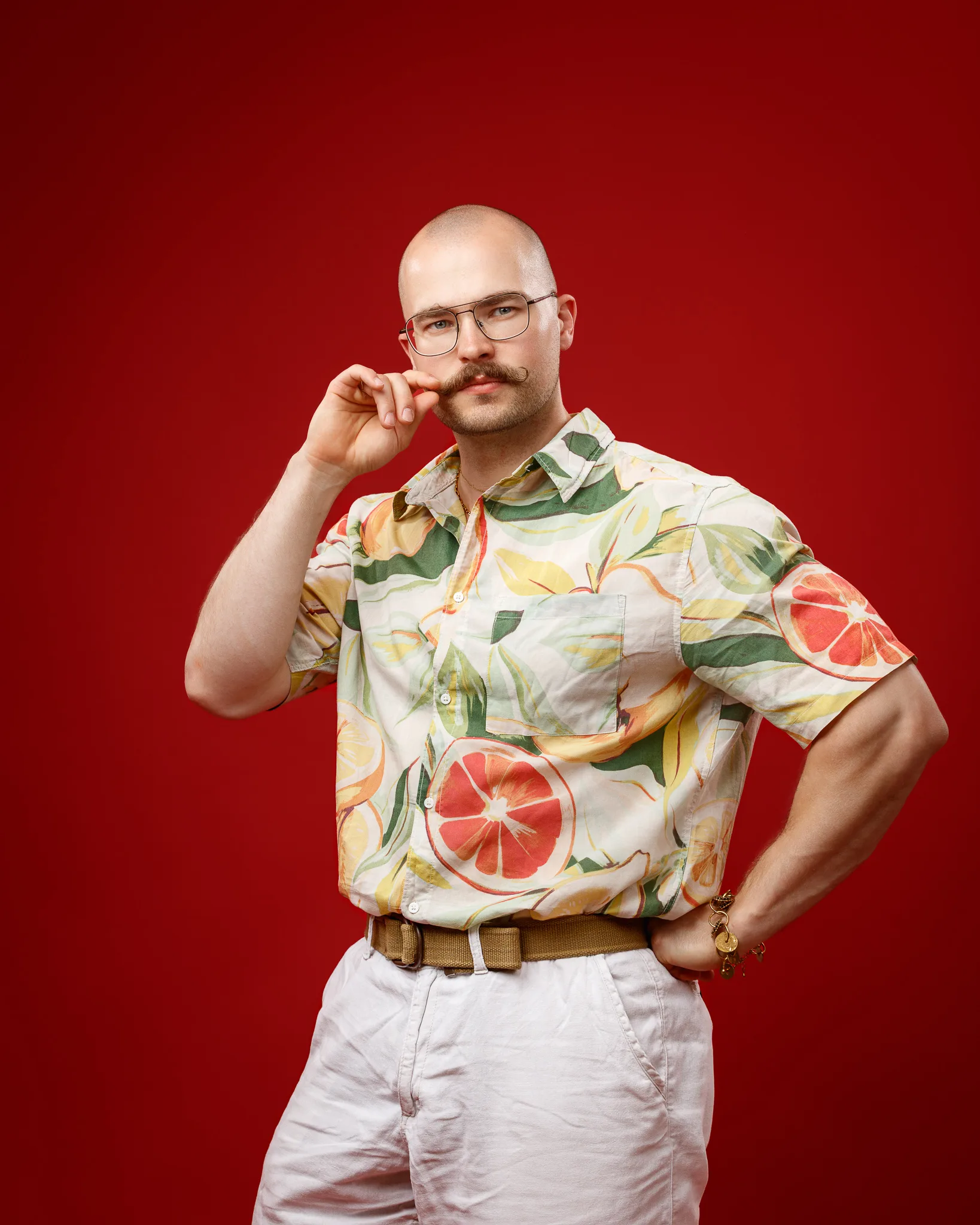 Man with glasses wearing fruit-patterned shirt against red background