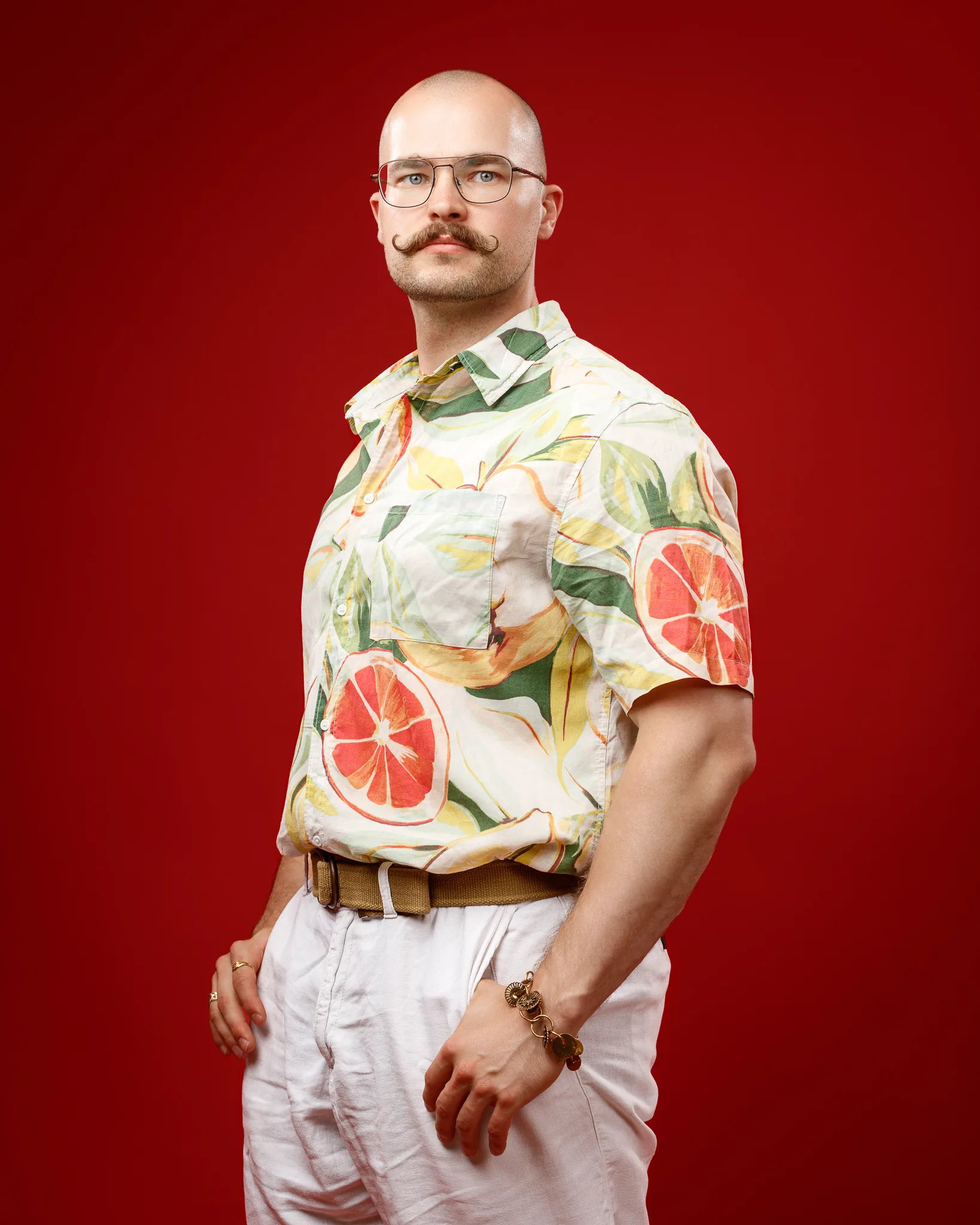 Man wearing fruit-patterned shirt and glasses against red background