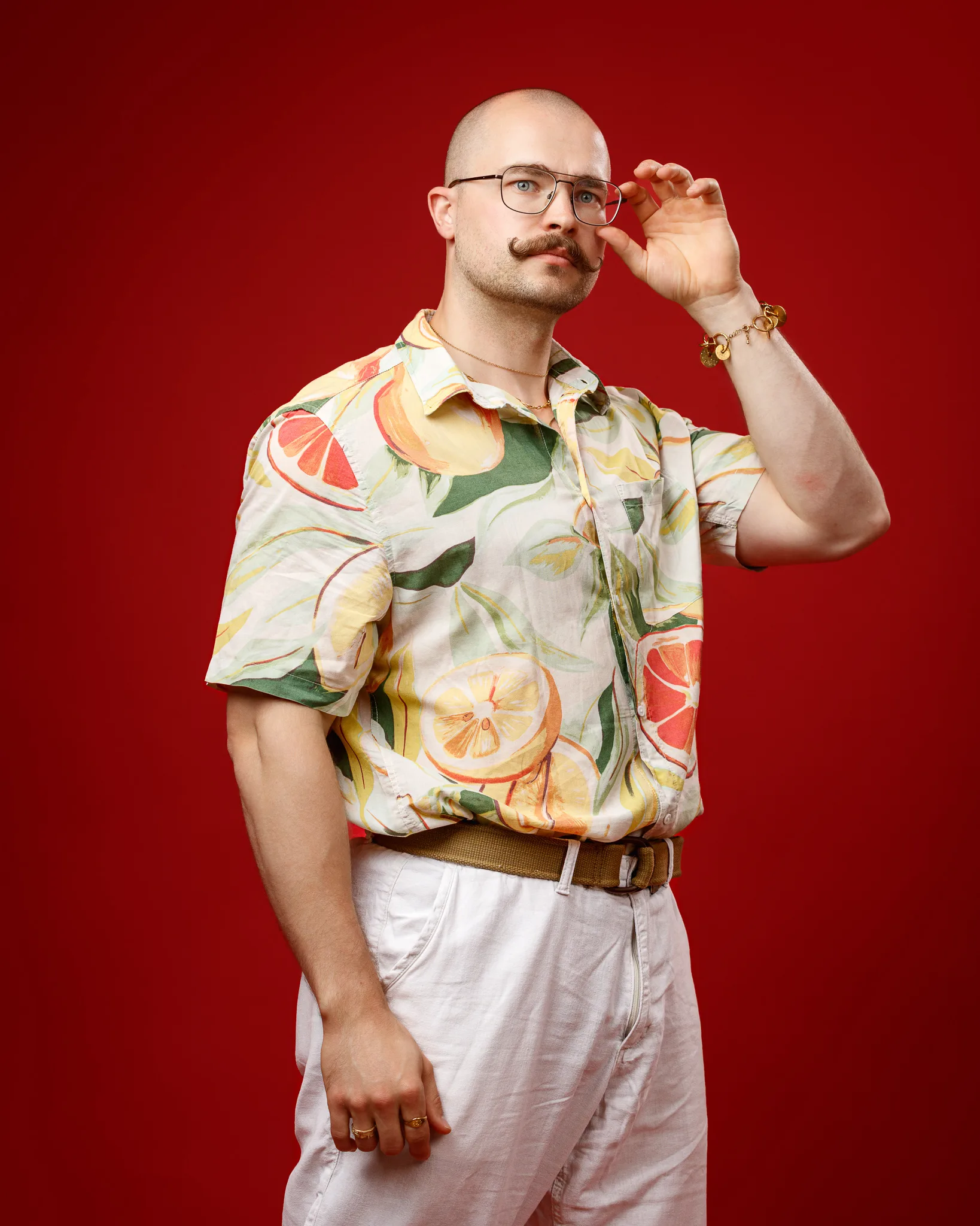 Man in colourful fruit-print shirt adjusting glasses against red background