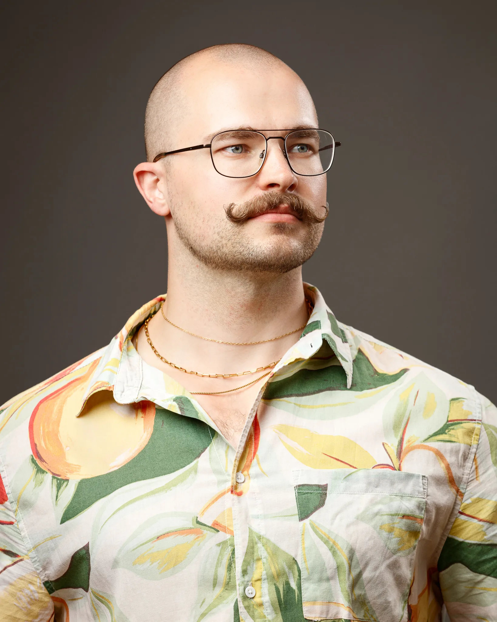 Bald man with mustache wearing glasses and patterned shirt