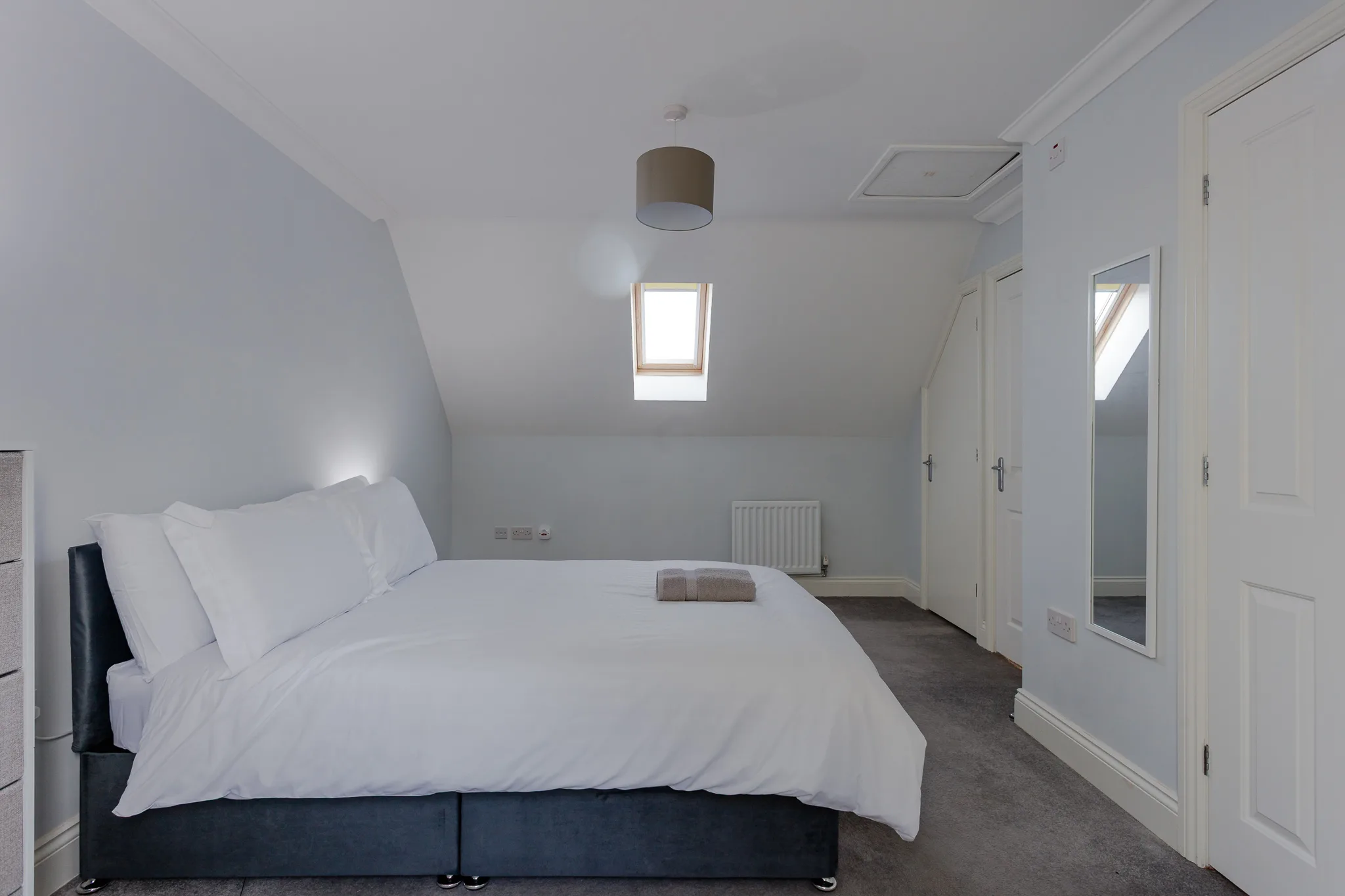 Modern attic bedroom with skylights, white walls and dark flooring